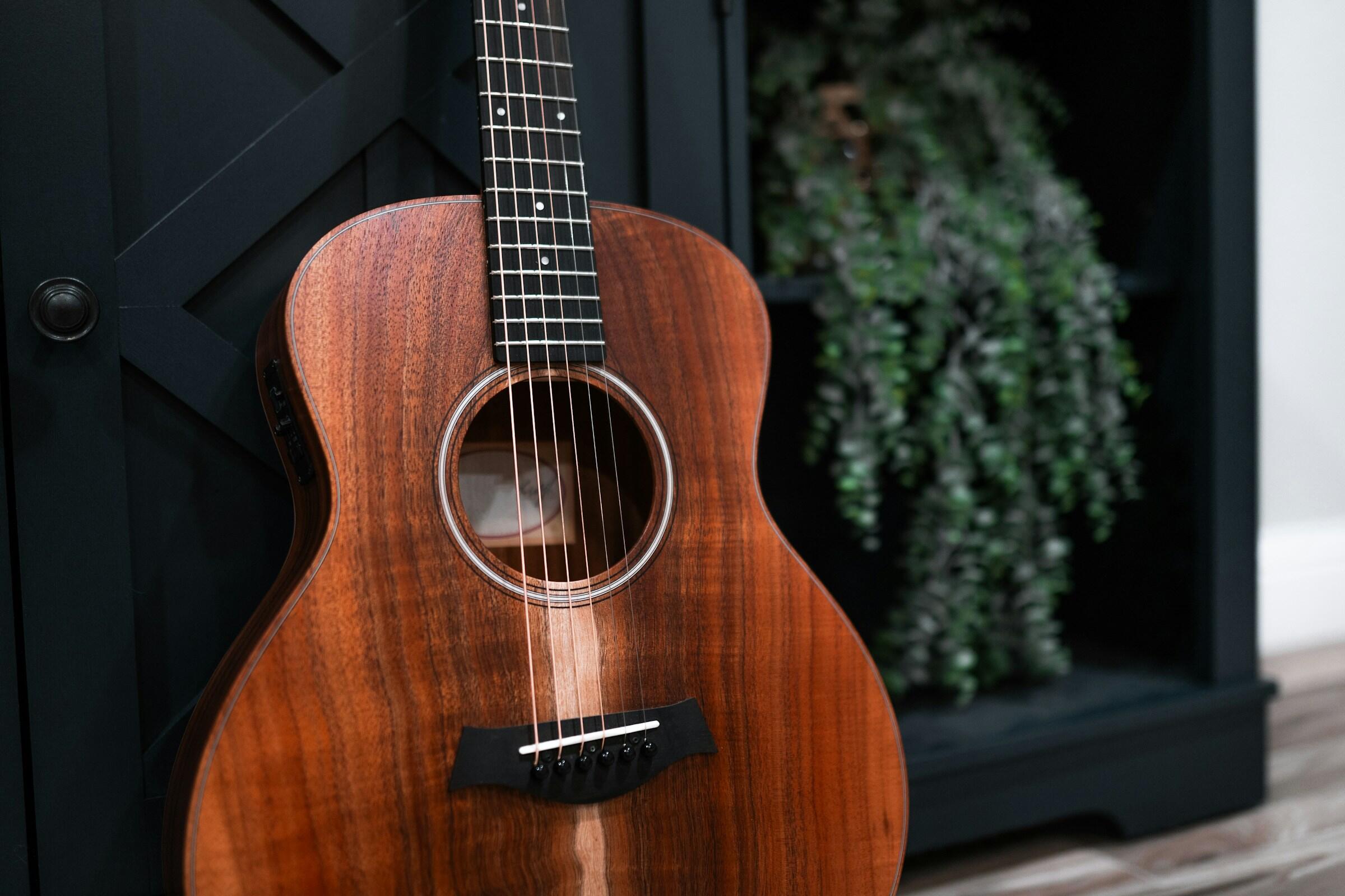 Primer plano de una hermosa guitarra acústica con un rico acabado de madera, apoyada sobre un mueble negro y vegetación.