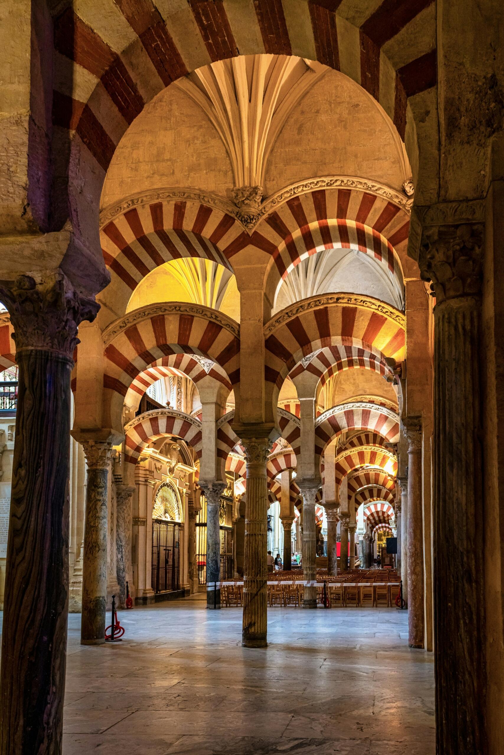 Arcos intrincados con rayas rojas y blancas en un vestíbulo histórico, mostrando una mezcla de estilos arquitectónicos y una suave iluminación ambiental en la mezquita de cordoba