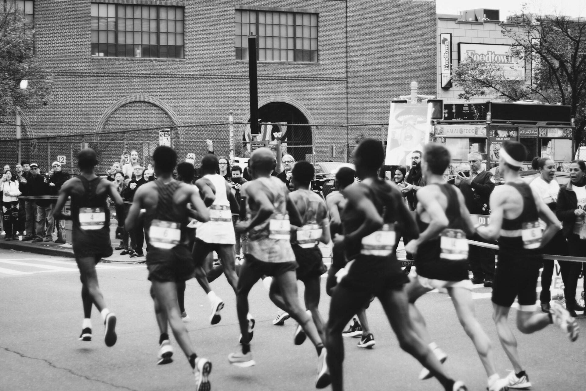 Un grupo de corredores compite en una carrera, mientras una animada multitud les anima en un entorno urbano.