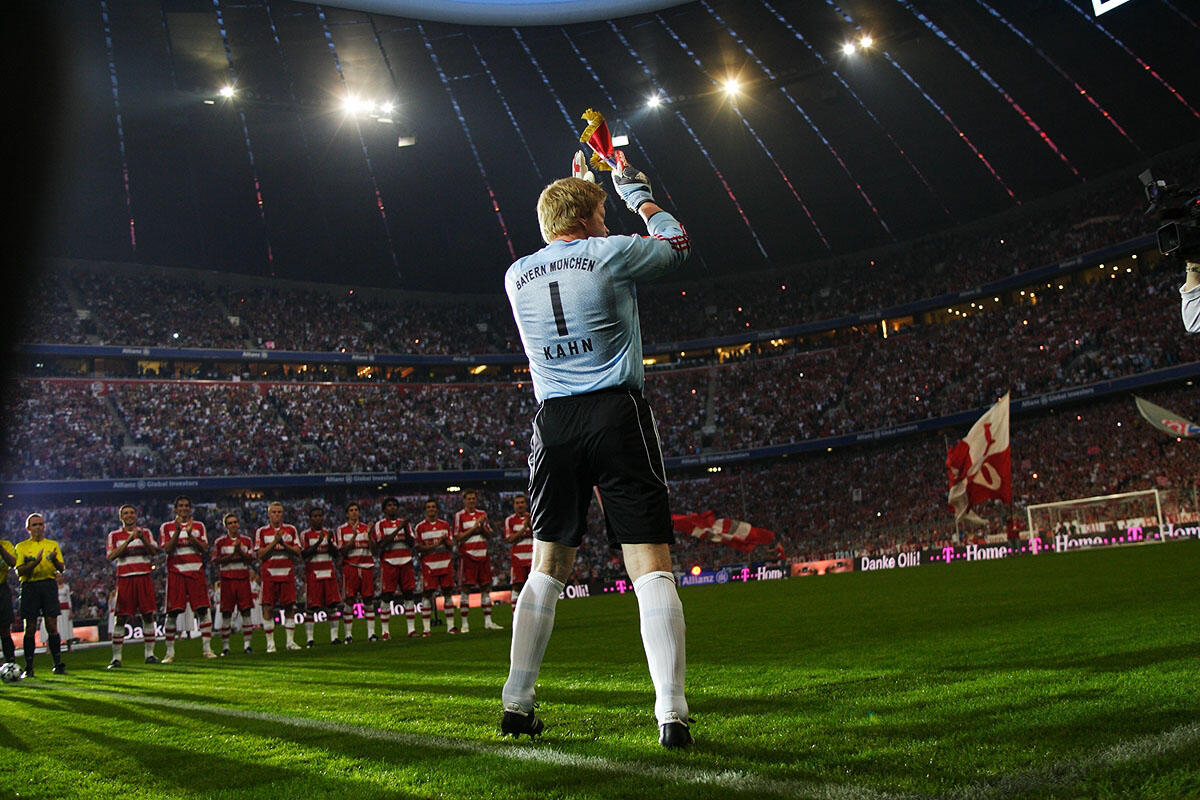 el portero del Bayern de Múnich Oliver Kahn gesticula con un trofeo, mientras los aficionados animan en un estadio repleto de banderas y luces de colores.