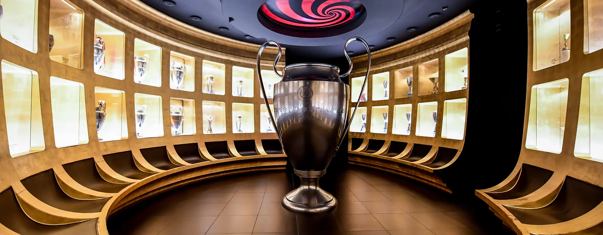 Un gran trofeo de la Liga de Campeones de la UEFA ocupa un lugar destacado en una sala circular, rodeado de vitrinas iluminadas en las paredes con los trofeos del ac milan
