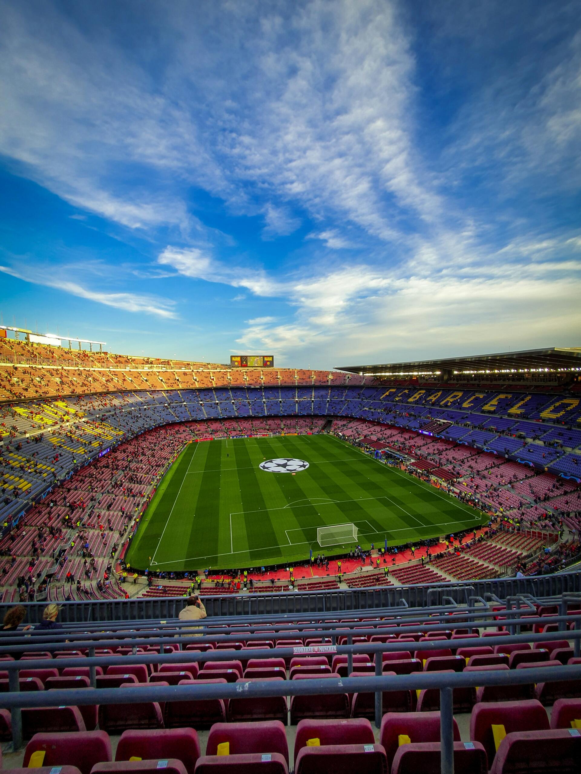 Una vista panorámica del estadio Camp Nou, asientos vacíos, un campo vibrante con el logotipo de la Liga de Campeones de la UEFA, bajo un cielo azul despejado.