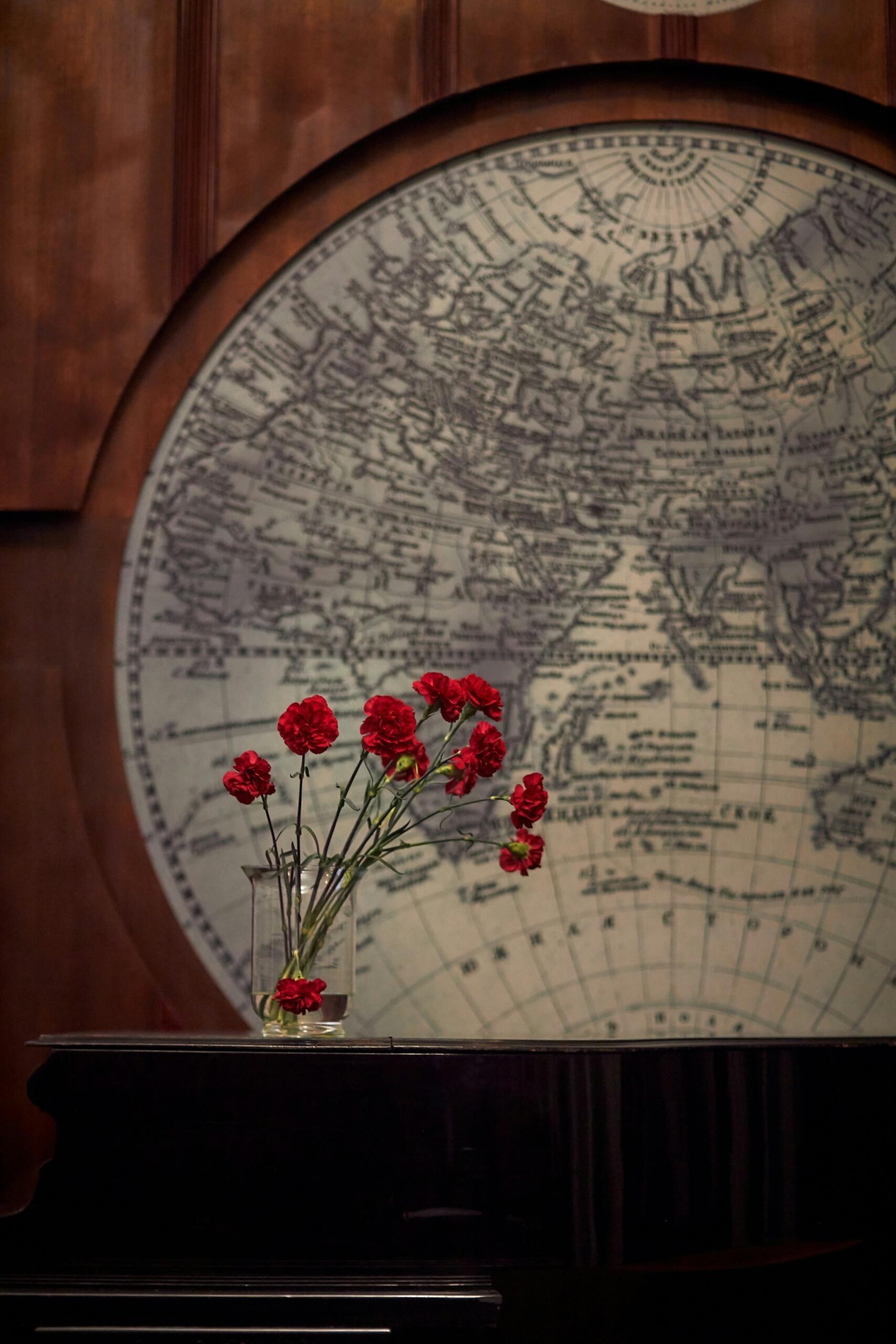 Un mapa y un jarrón con flores rojas sobre una mesa.