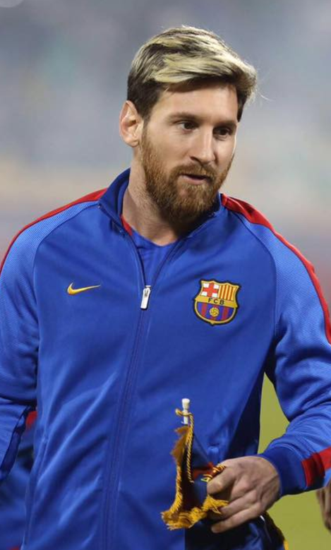 el jugador de fútbol leo mesi con una chaqueta azul del FC Barcelona sale del campo con un trofeo dorado en la mano.