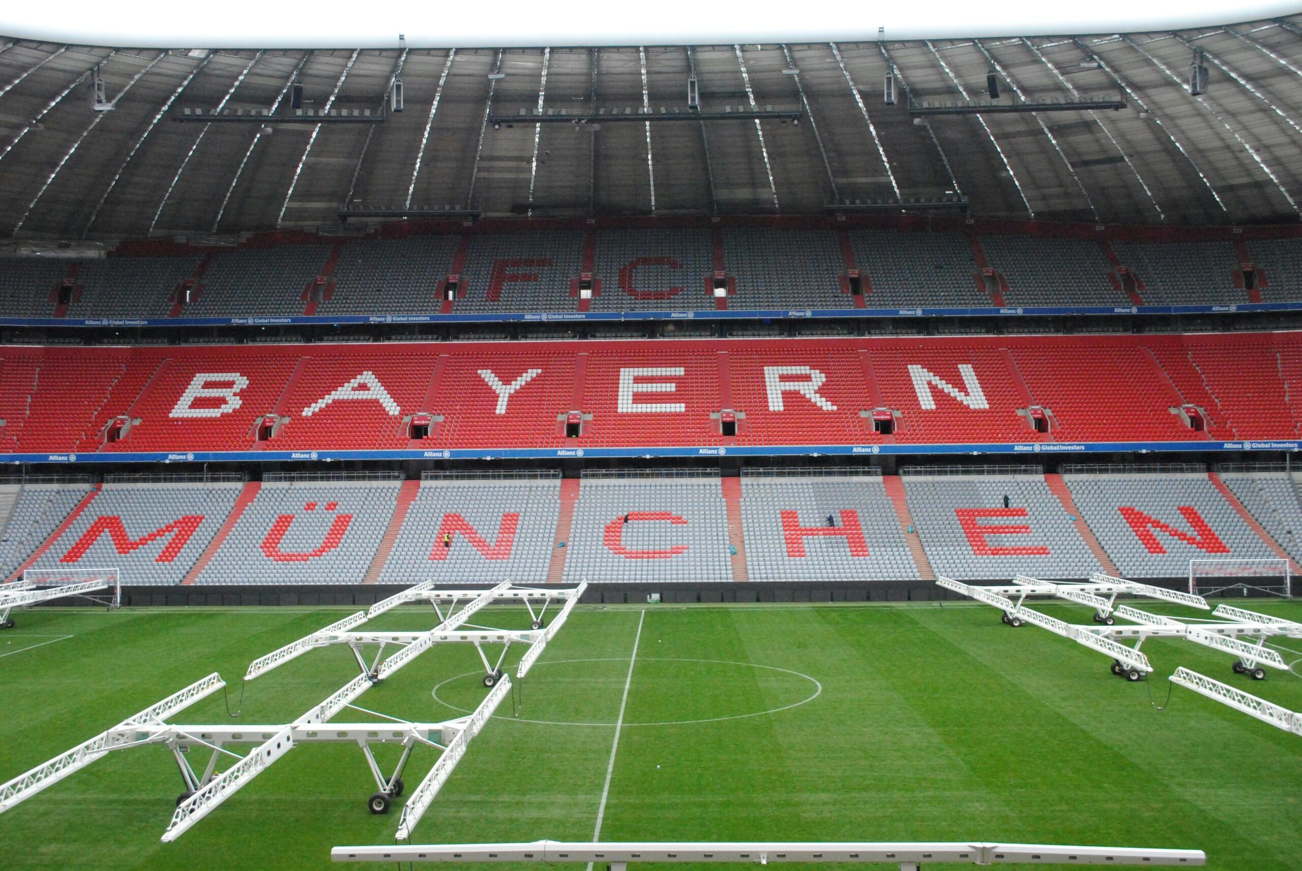Vista interior del estadio del Bayern de Múnich, con grandes letras rojas y blancas y equipos de mantenimiento en el campo verde.