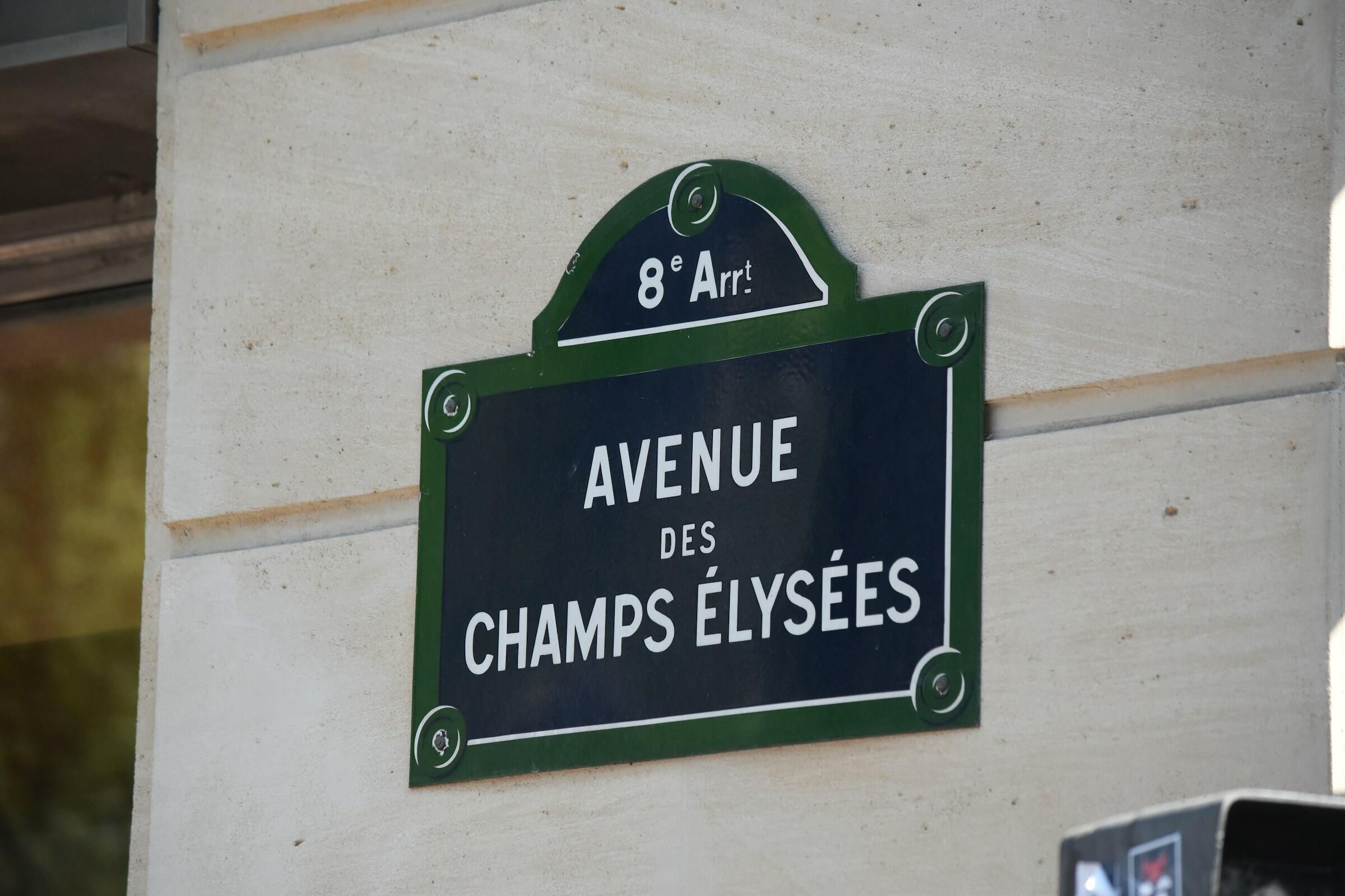Señal de tráfico con la inscripción «Avenue des Champs Élysées» situada en el distrito 8 de París, adosada a una pared luminosa.