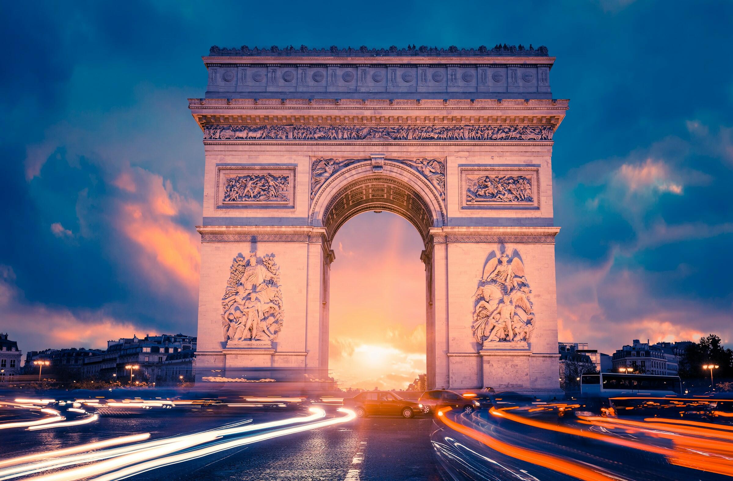 El Arco del Triunfo de París resplandece en un dramático atardecer, con las borrosas luces de los coches rodeando el monumento en movimiento.