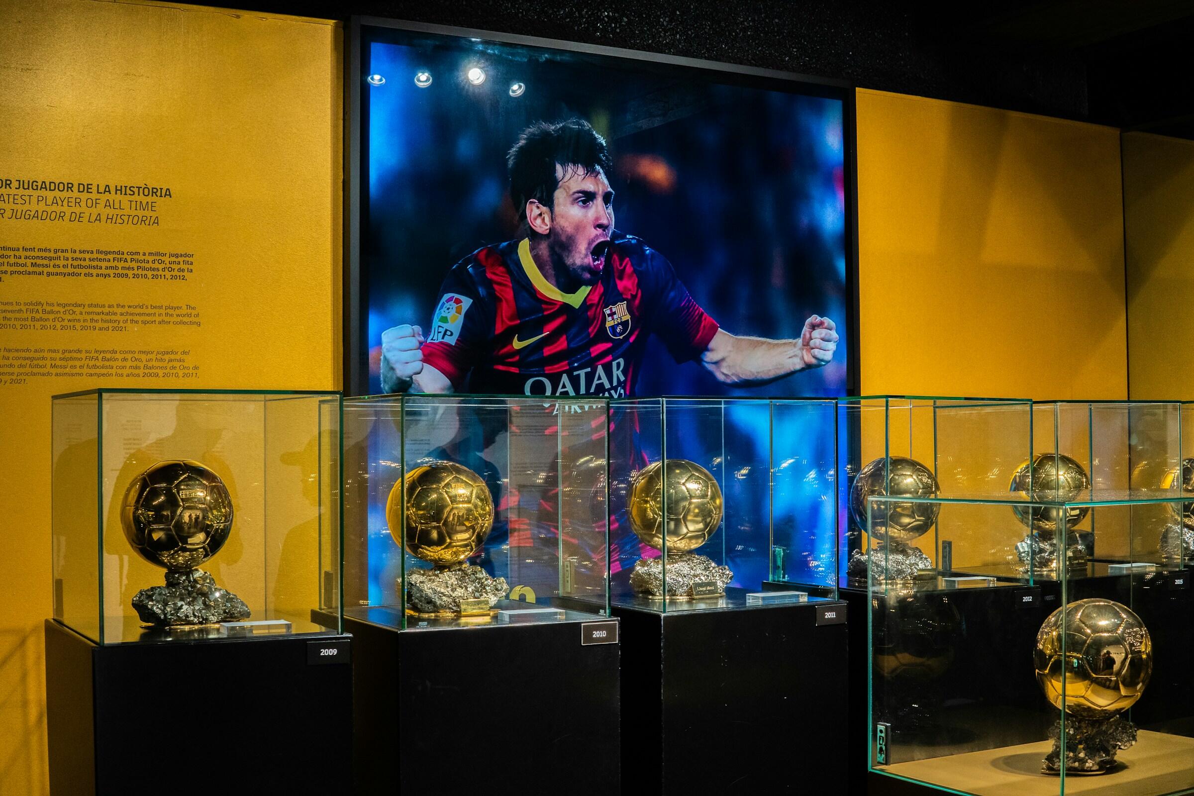 Expositor de múltiples trofeos del Balón de Oro con una imagen destacada de un célebre futbolista con la camiseta del Barcelona.