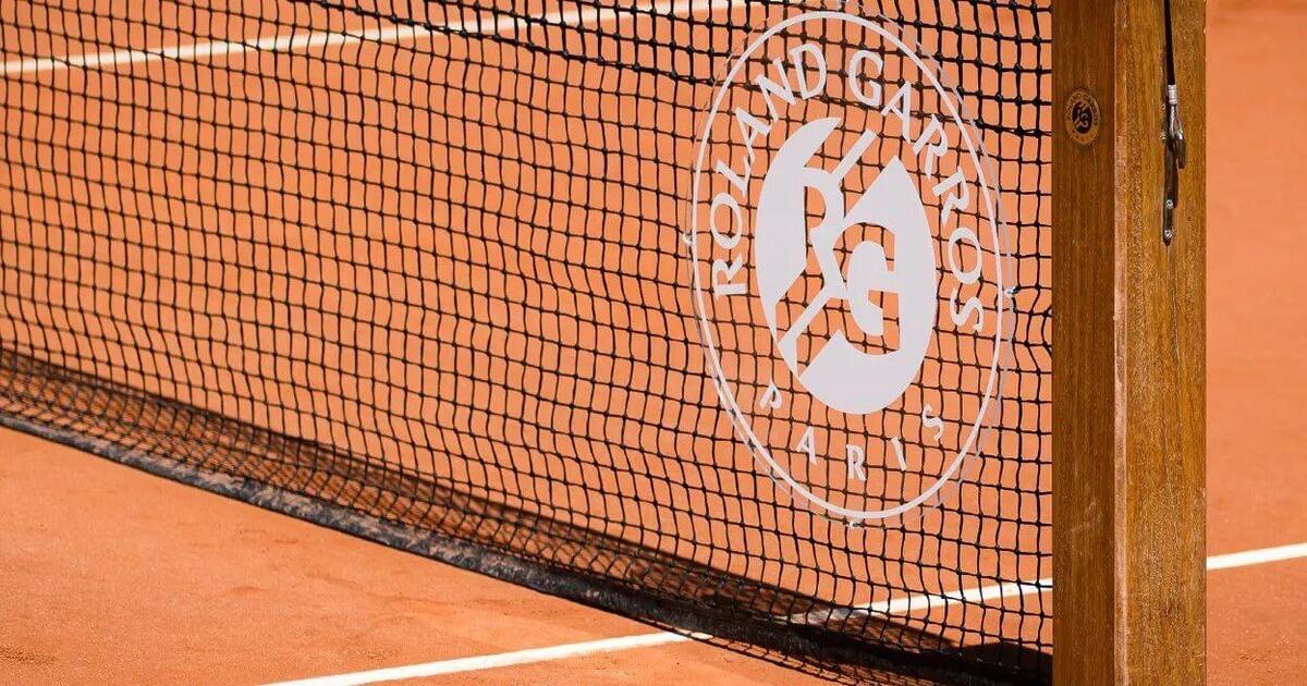 Primer plano de una red de tenis en una pista de tierra batida con el logotipo de Roland Garros, en el que aparecen las siglas «RG» y la palabra «París», lo que hace referencia a un prestigioso torneo de tenis.