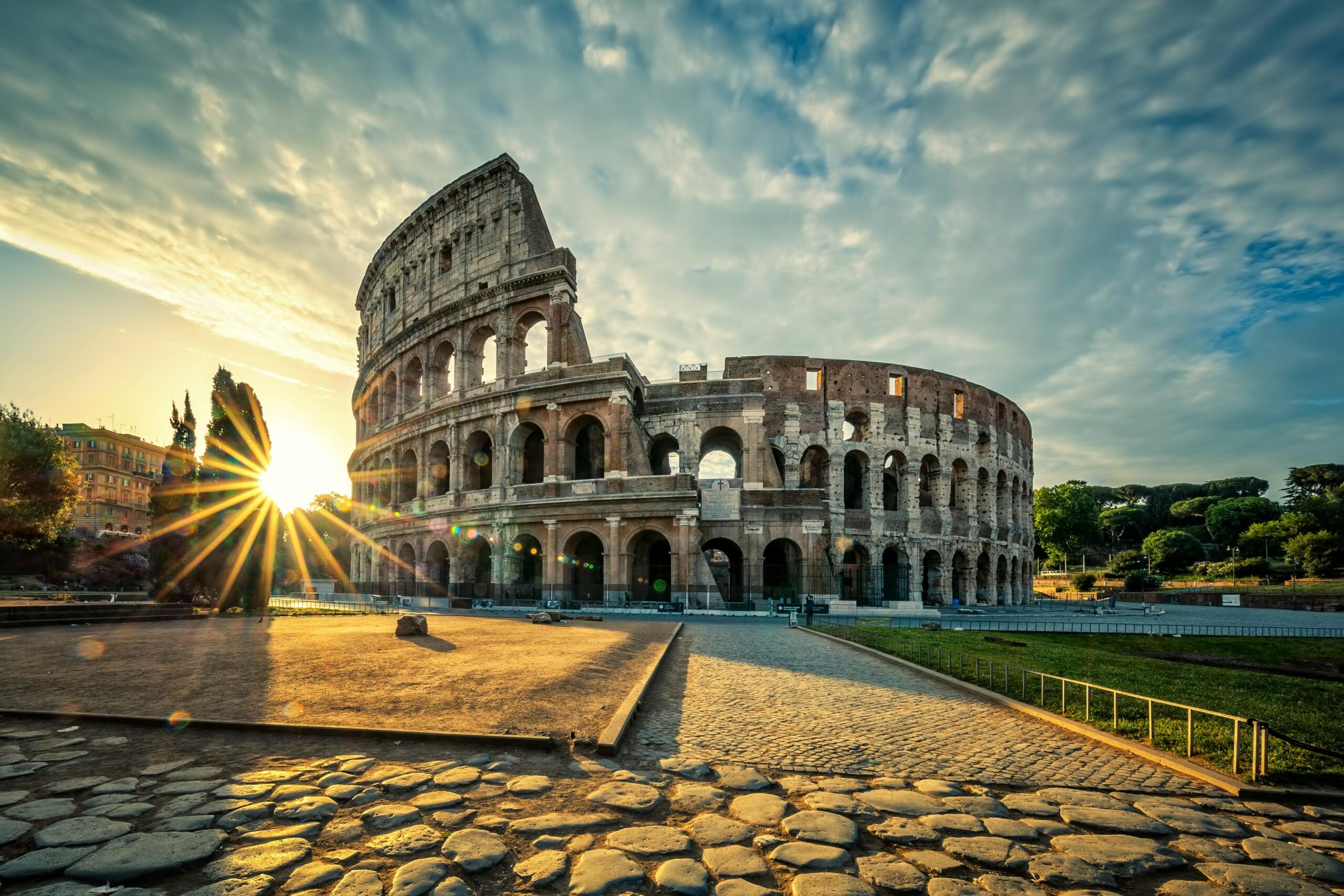 El Coliseo de Roma bañado por la luz dorada del sol, rodeado de exuberante vegetación y un cielo espectacular.