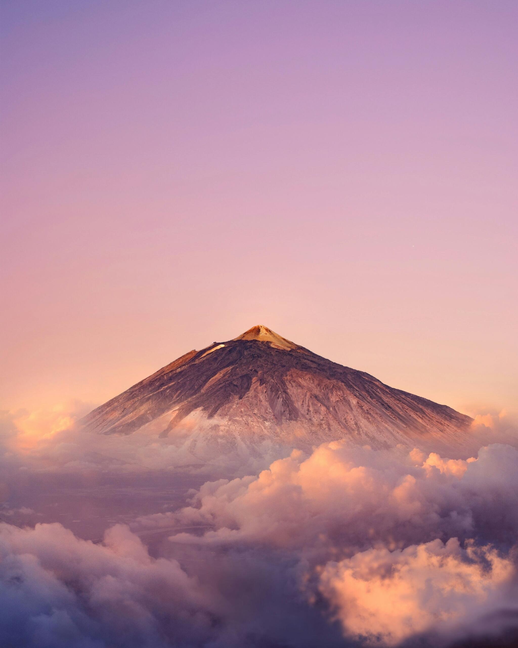 El majestuoso volcán teide se eleva sobre las suaves nubes al amanecer, iluminado por un cielo cálido y pastel, mostrando la serena belleza de la naturaleza.