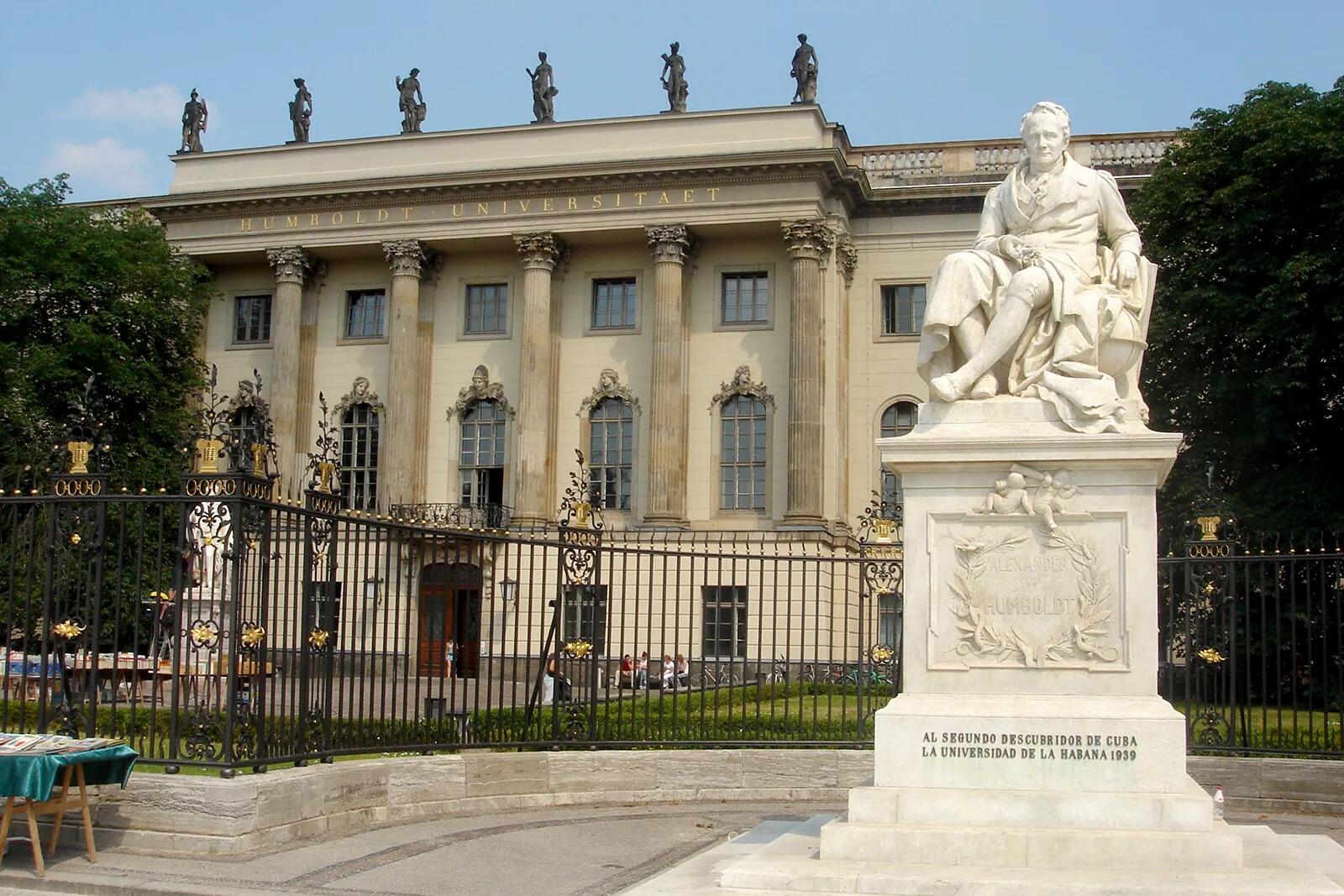 Estatua de una figura sentada frente al edificio de la Universidad Humboldt de Berlín. Se aprecia la fachada neoclásica con columnas, que le confiere un aire de grandeza.