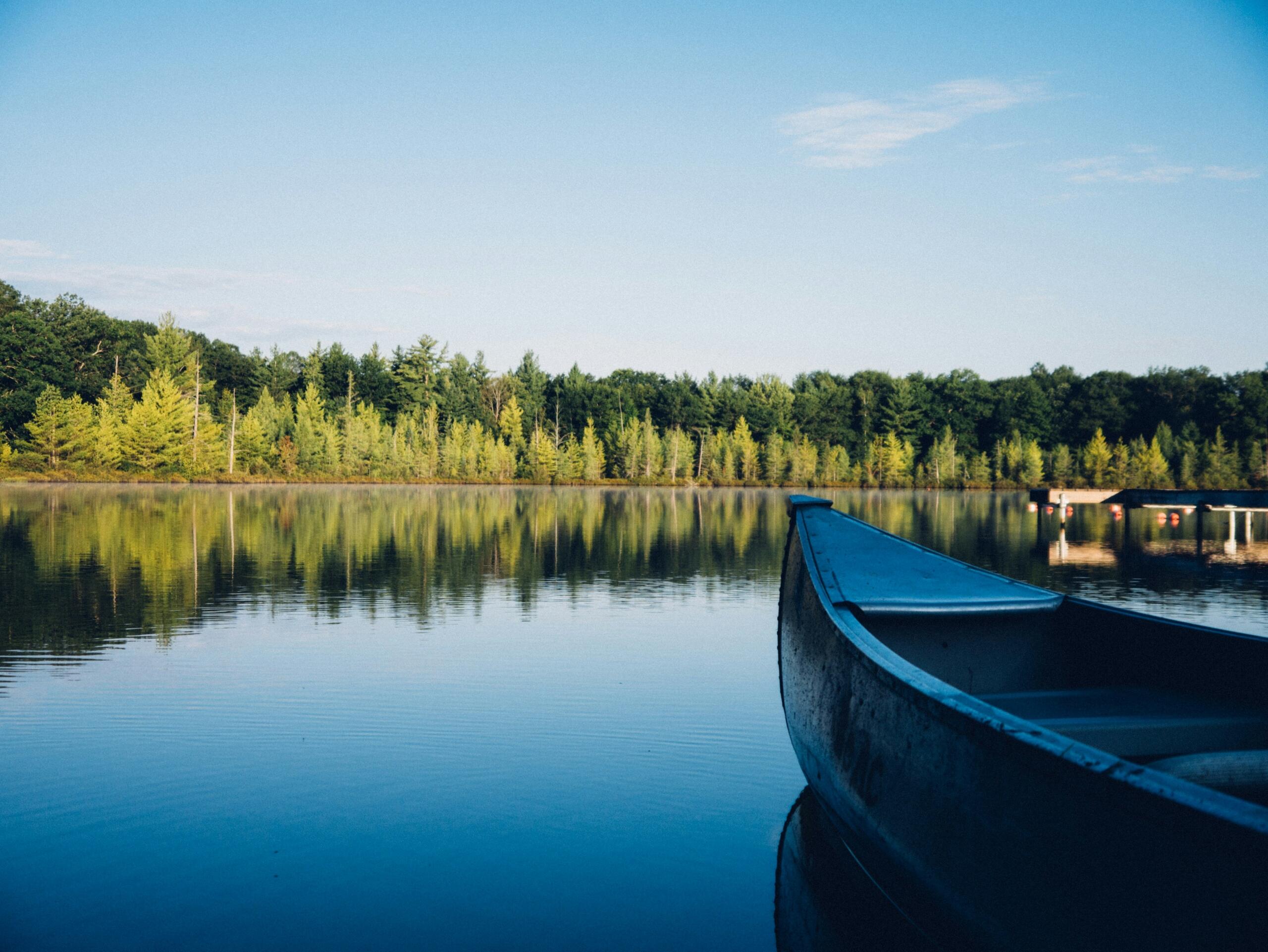 Una serena escena lacustre con una canoa azul en primer plano, que refleja frondosos árboles verdes y un cielo azul despejado.