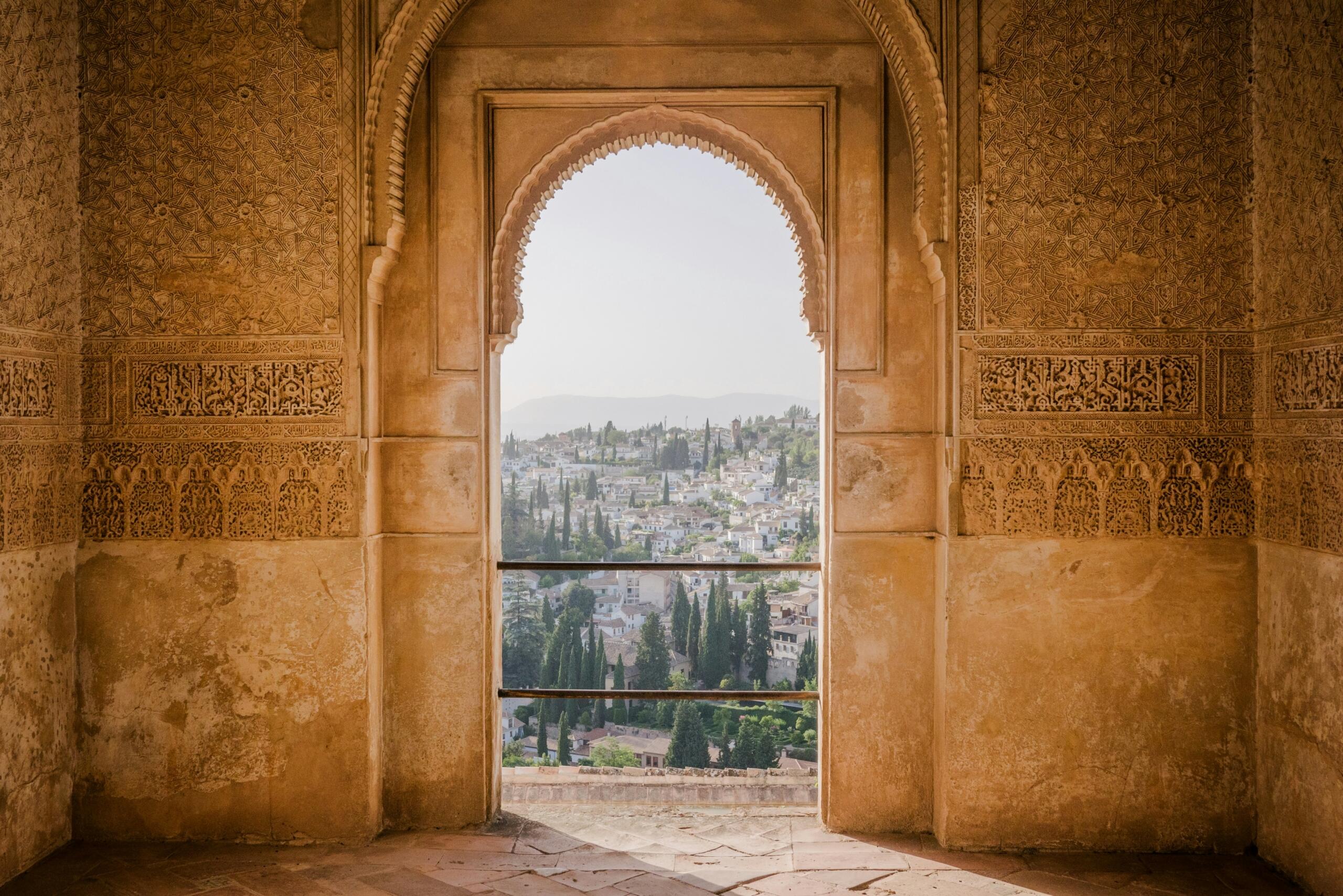 Intrincado arco que revela una vista panorámica de la ciudad de granada y la ladera de una colina, enmarcada por tallas de piedra ornamentadas de la Alhambra con una suave luz natural.
