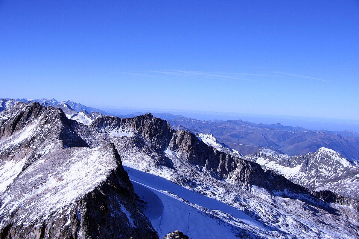 Una vista panorámica de montañas nevadas del aneto  bajo un cielo azul despejado, que muestra picos escarpados y cordilleras lejanas.