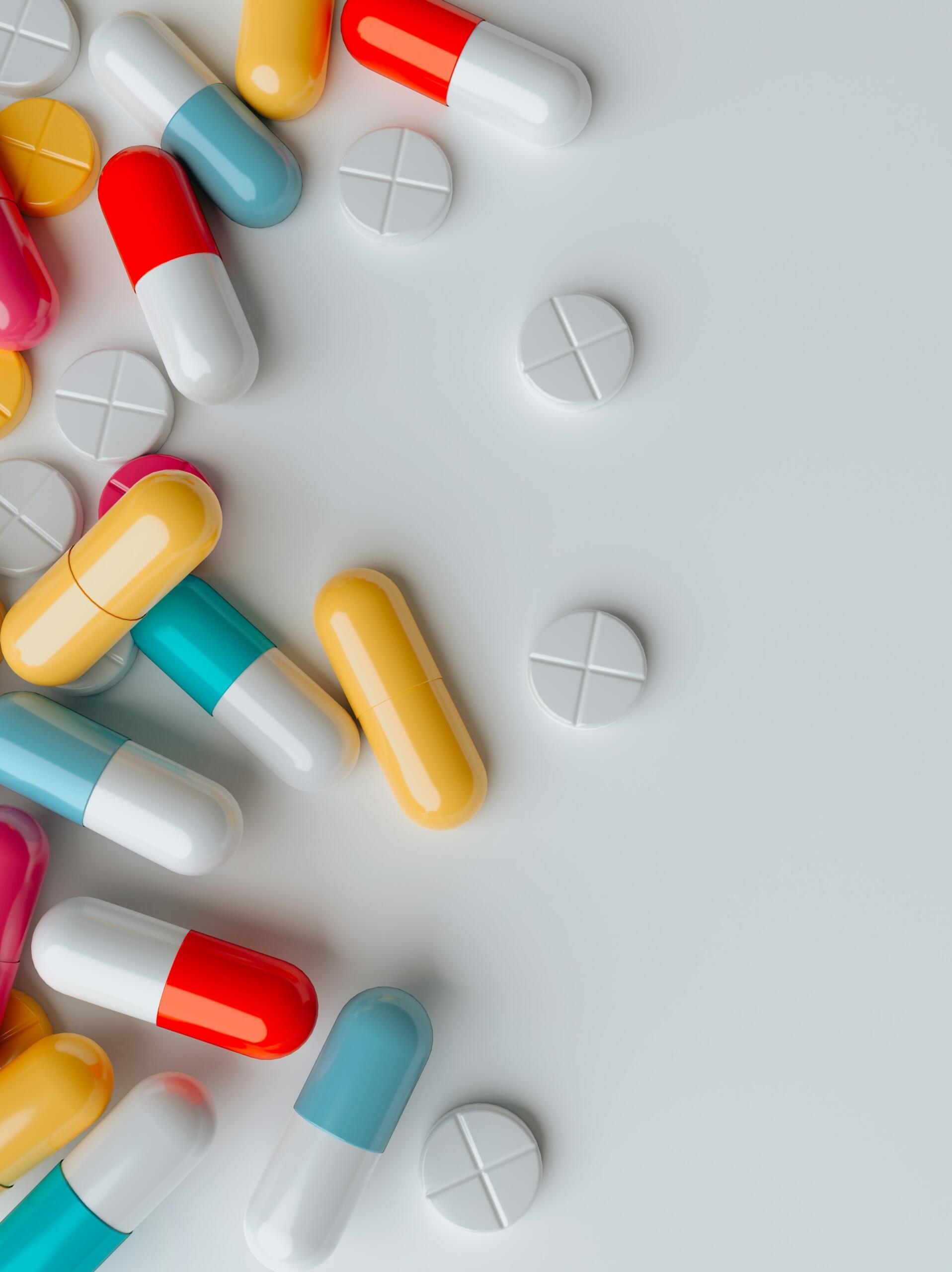 Una variedad de cápsulas de colores y comprimidos redondos esparcidos sobre una superficie clara, mostrando diferentes formas y colores de medicamentos.