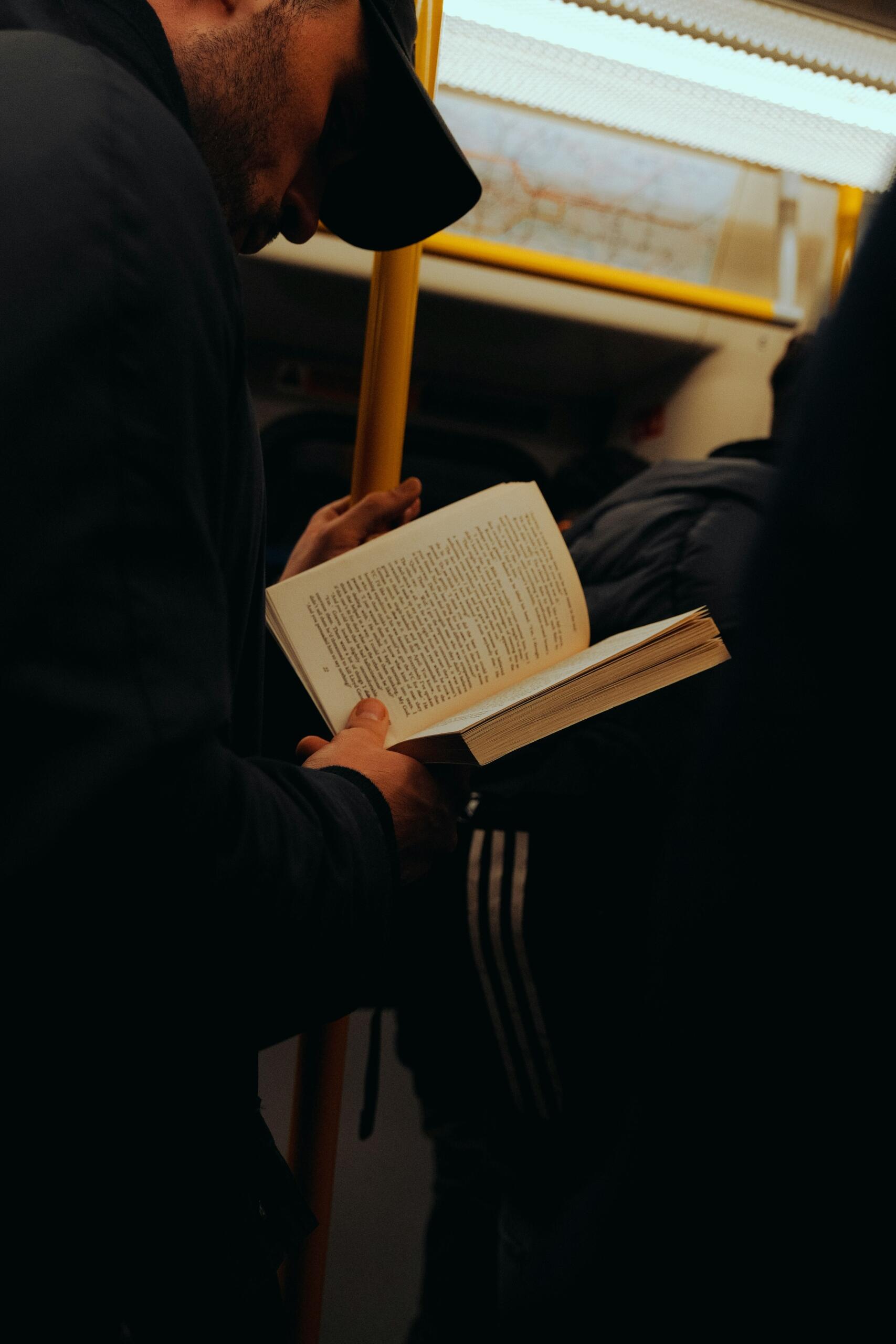 Un hombre lee un libro mientras viaja en un tren de metro.
