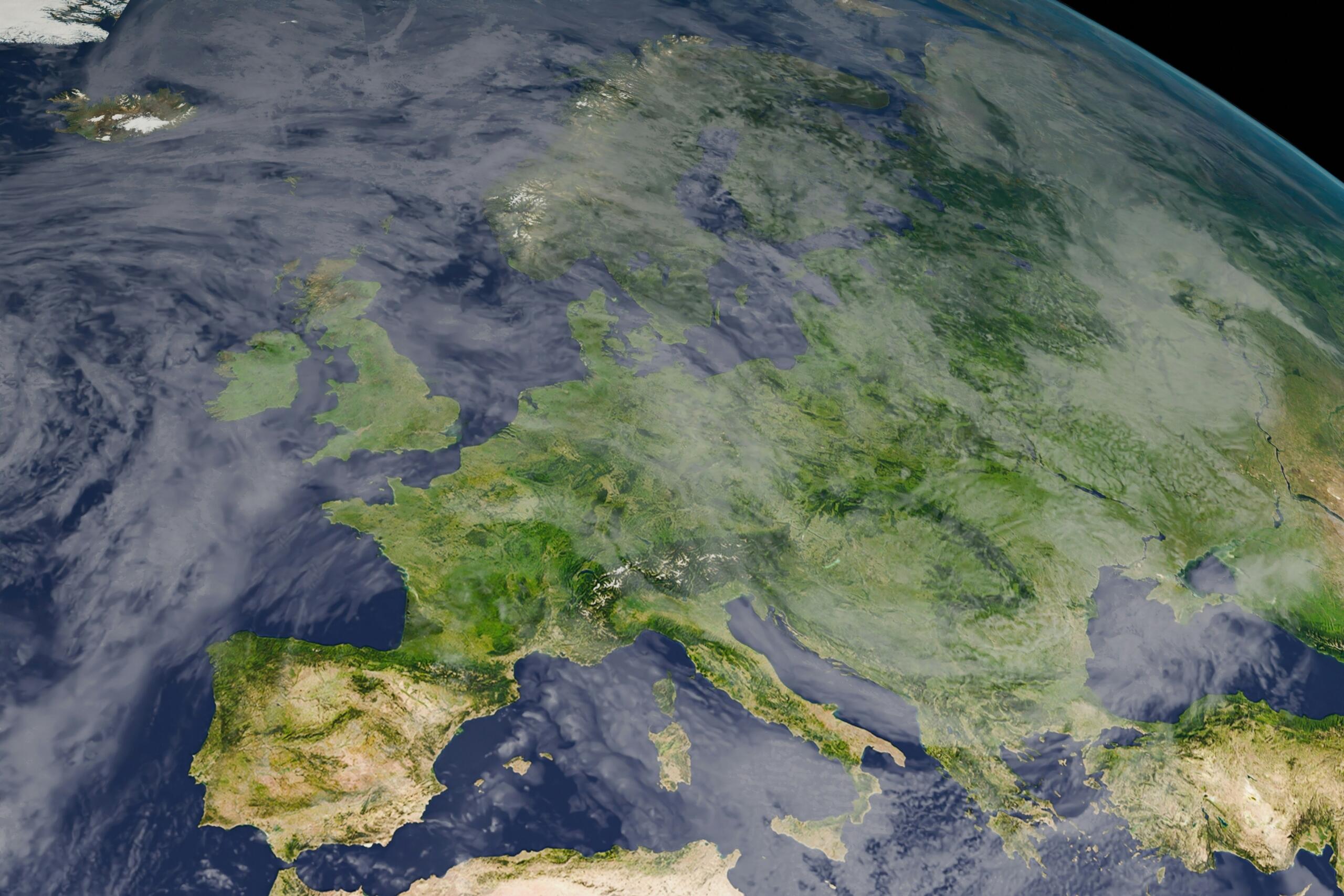 Vista por satélite de Europa que muestra exuberantes paisajes, cadenas montañosas y aguas circundantes, con nubes que oscurecen parcialmente el cielo.