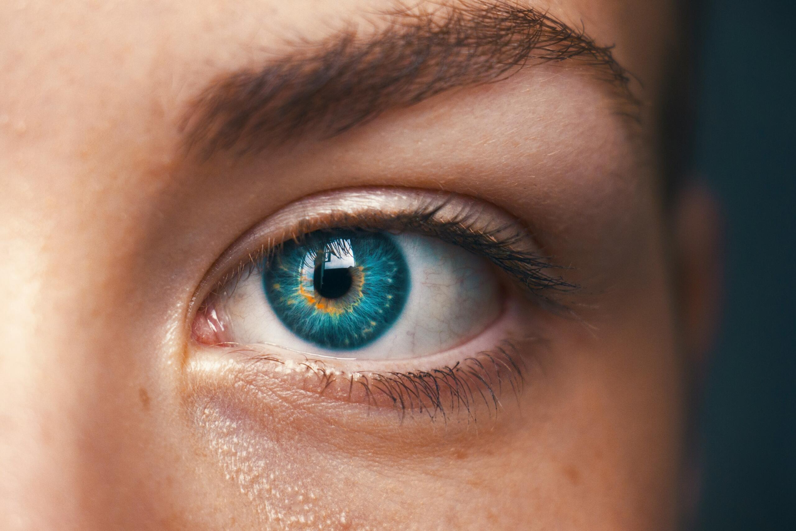 Un primer plano de un llamativo ojo azul con detalles intrincados, que presenta colores vibrantes y reflejos, destacando las pestañas y la textura de la piel.