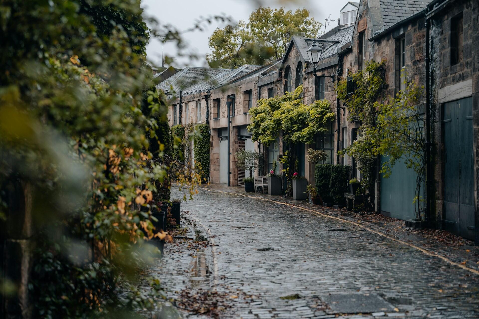 Un callejón empedrado bordeado de edificios de piedra y exuberante vegetación, que crea un ambiente sereno y pintoresco.