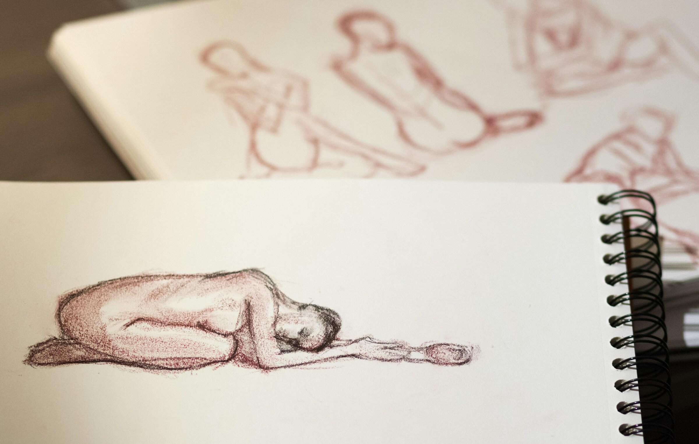 Boceto de una figura desnuda en posición fetal, con otros dibujos inacabados de poses visibles en el fondo.