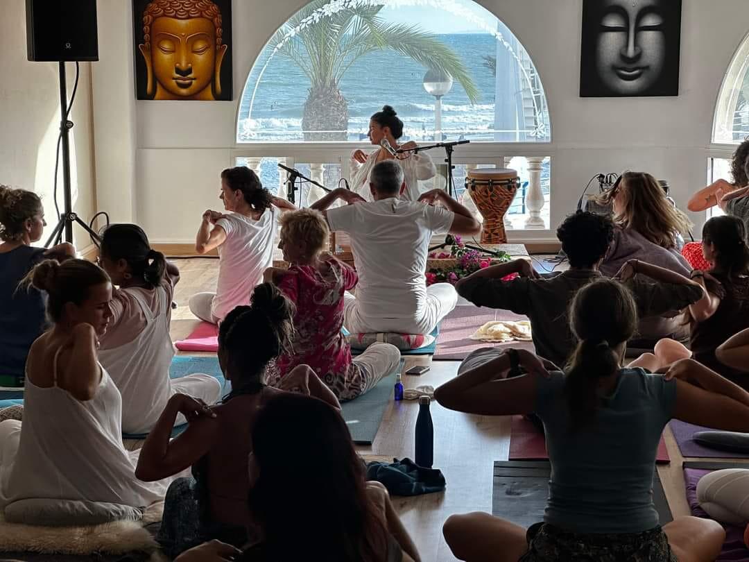 Un grupo de personas practicando yoga en un estudio sereno con vistas al mar en santa pola alicante, rodeado de decoración tropical y un ambiente tranquilo.