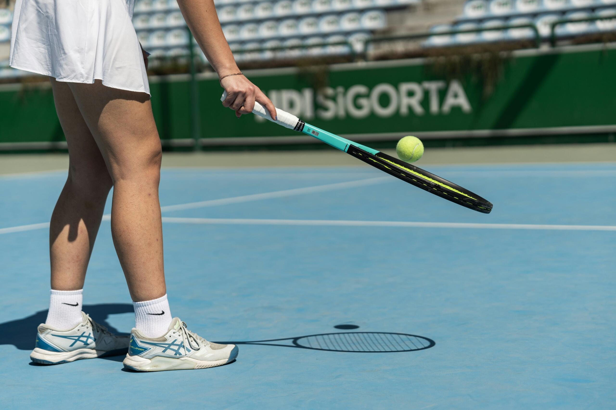 Mujer con vestido blanco sosteniendo una raqueta de tenis, lista para jugar en una cancha al aire libre.