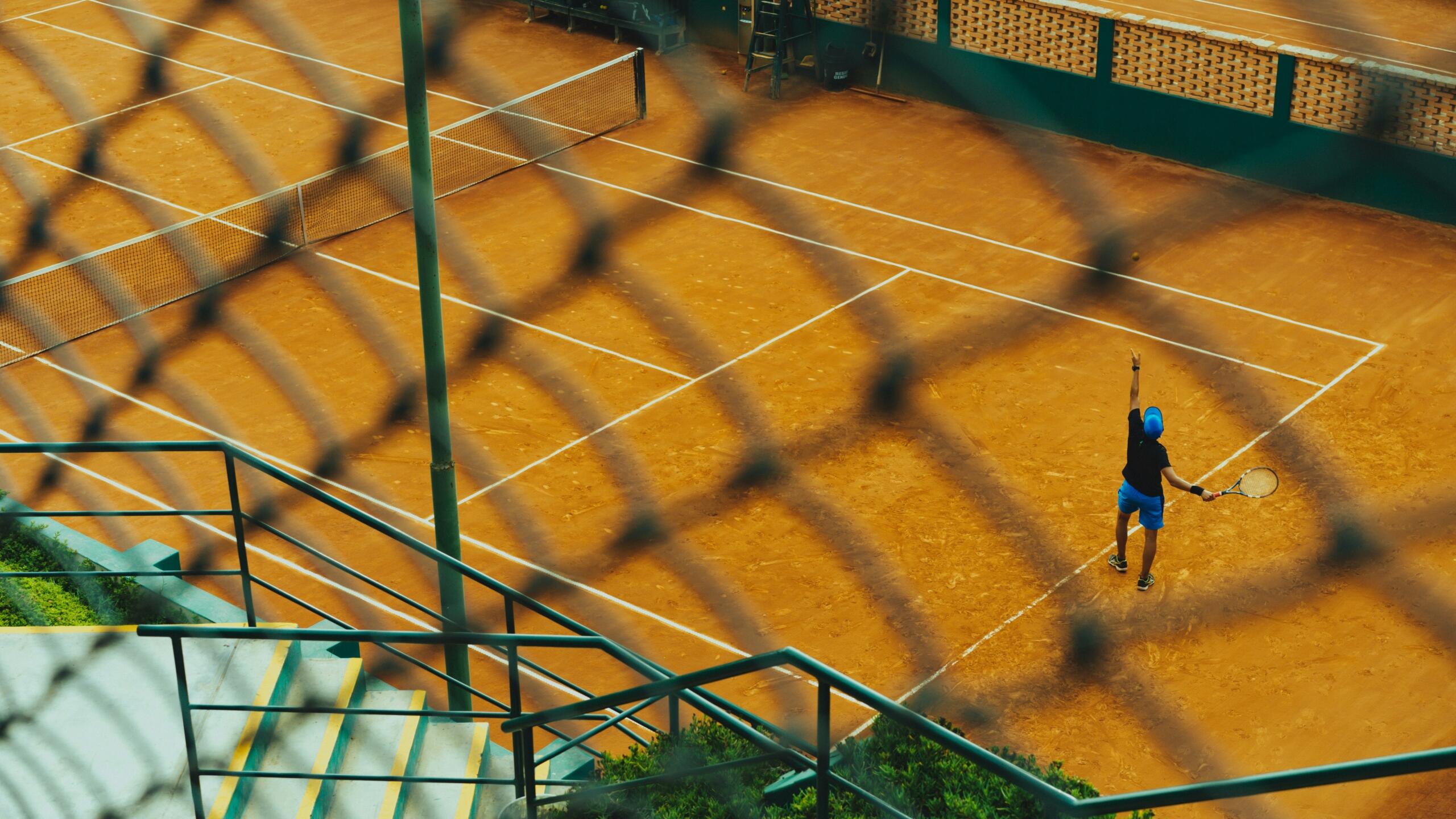 Jugador de tenis en una cancha de arcilla, preparado para realizar un saque.