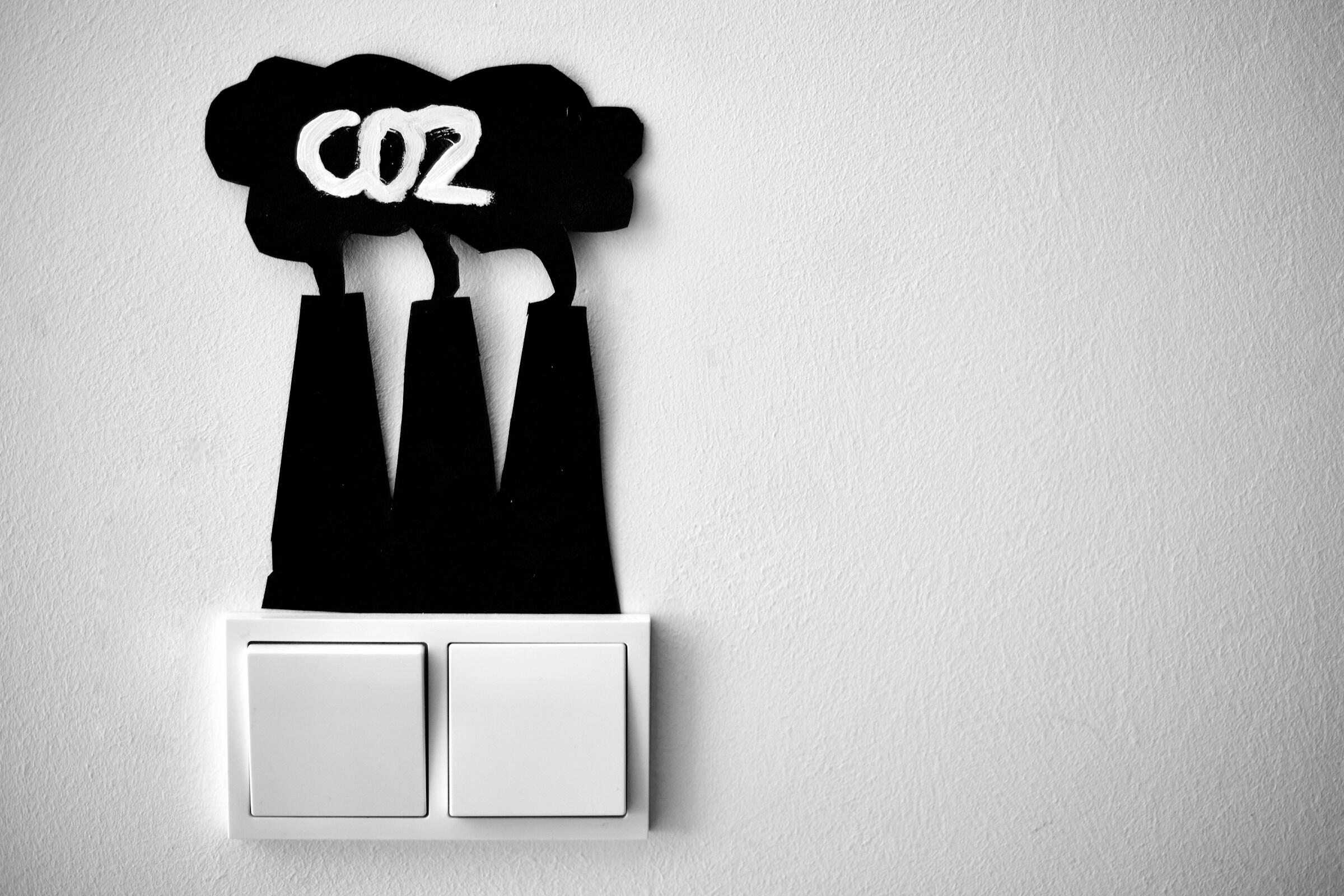 Una decoración minimalista para la pared muestra tres chimeneas negras con la inscripción «CO2» encima, situadas sobre un interruptor de luz blanco.