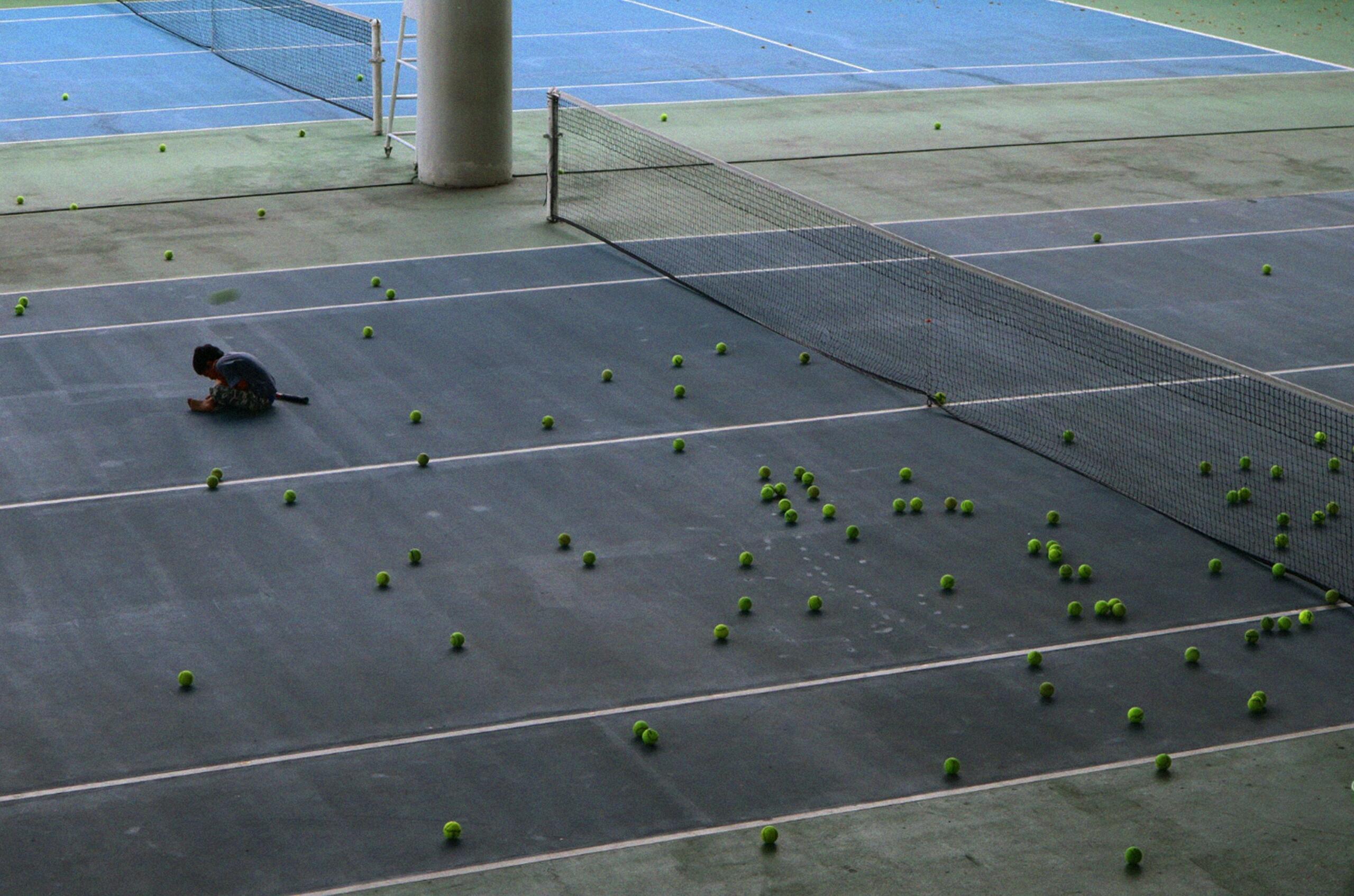 Una cancha de tenis con una persona sentada en el suelo, observando el juego desde una posición relajada.