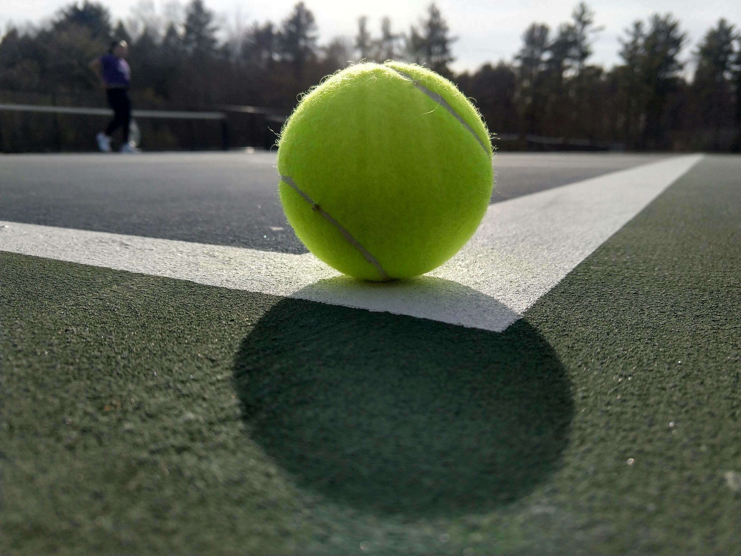 Una pelota de tenis sobre una cancha de tenis, con líneas marcadas y fondo verde.