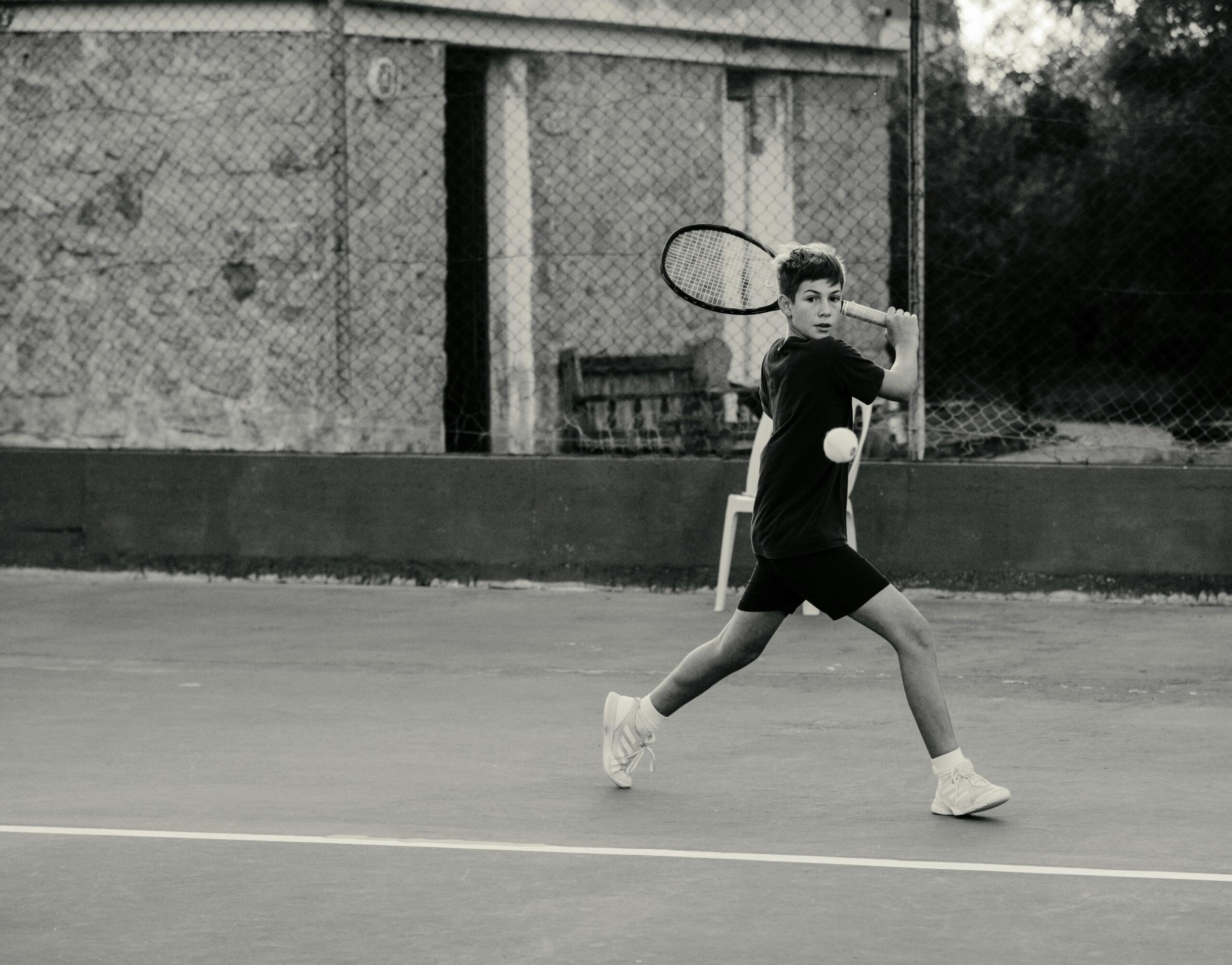 Hombre jugando al tenis en una cancha, sosteniendo una raqueta y preparado para golpear la pelota. 