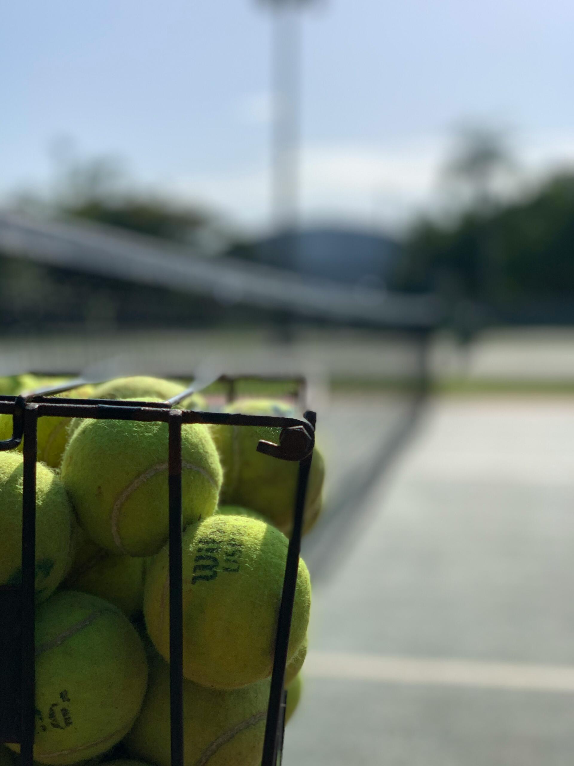 Una cesta de pelotas de tenis sobre una cancha de tenis.