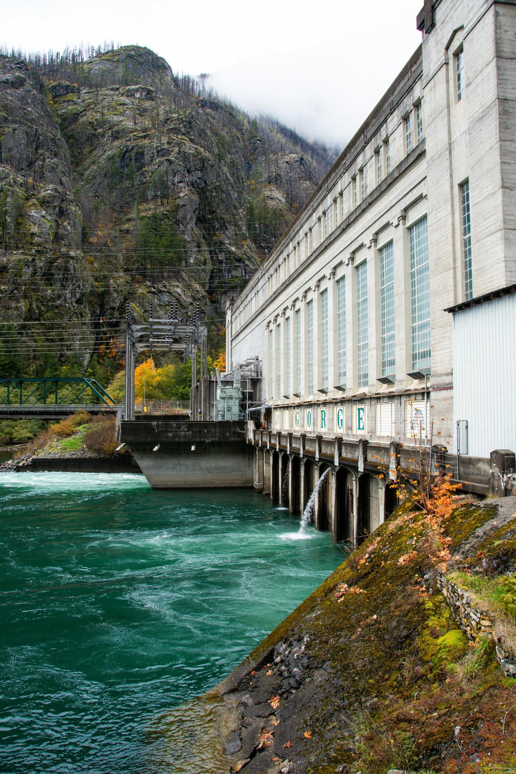 La presa Gorge, rodeada de terreno rocoso y un río, presenta una estructura de hormigón con grandes ventanas y agua fluyendo por debajo.