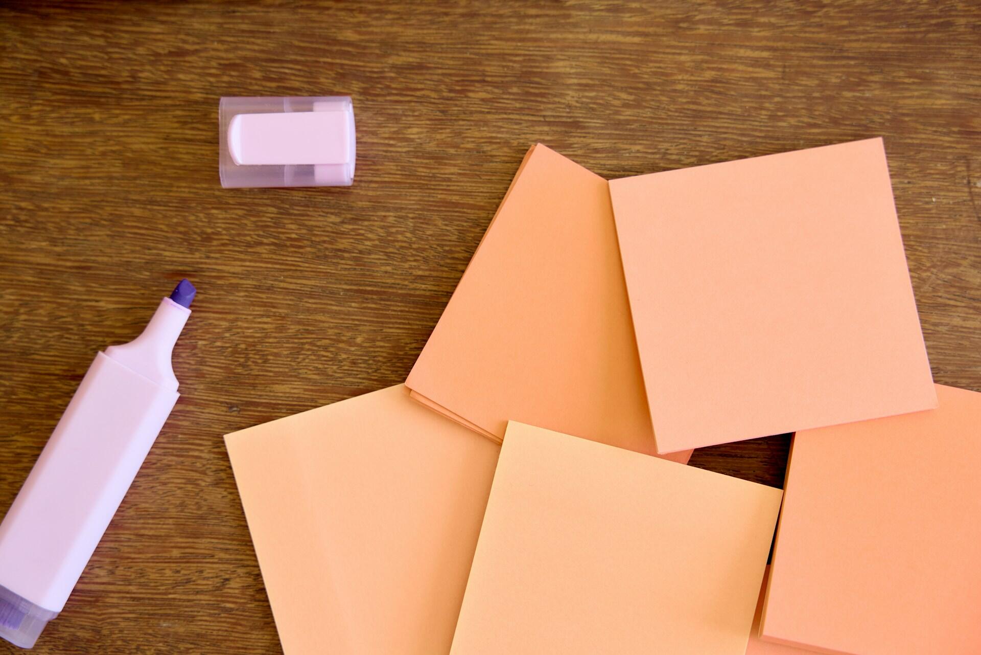 Una colección de notas adhesivas naranjas, un marcador morado y una goma de borrar sobre la superficie de una mesa de madera.