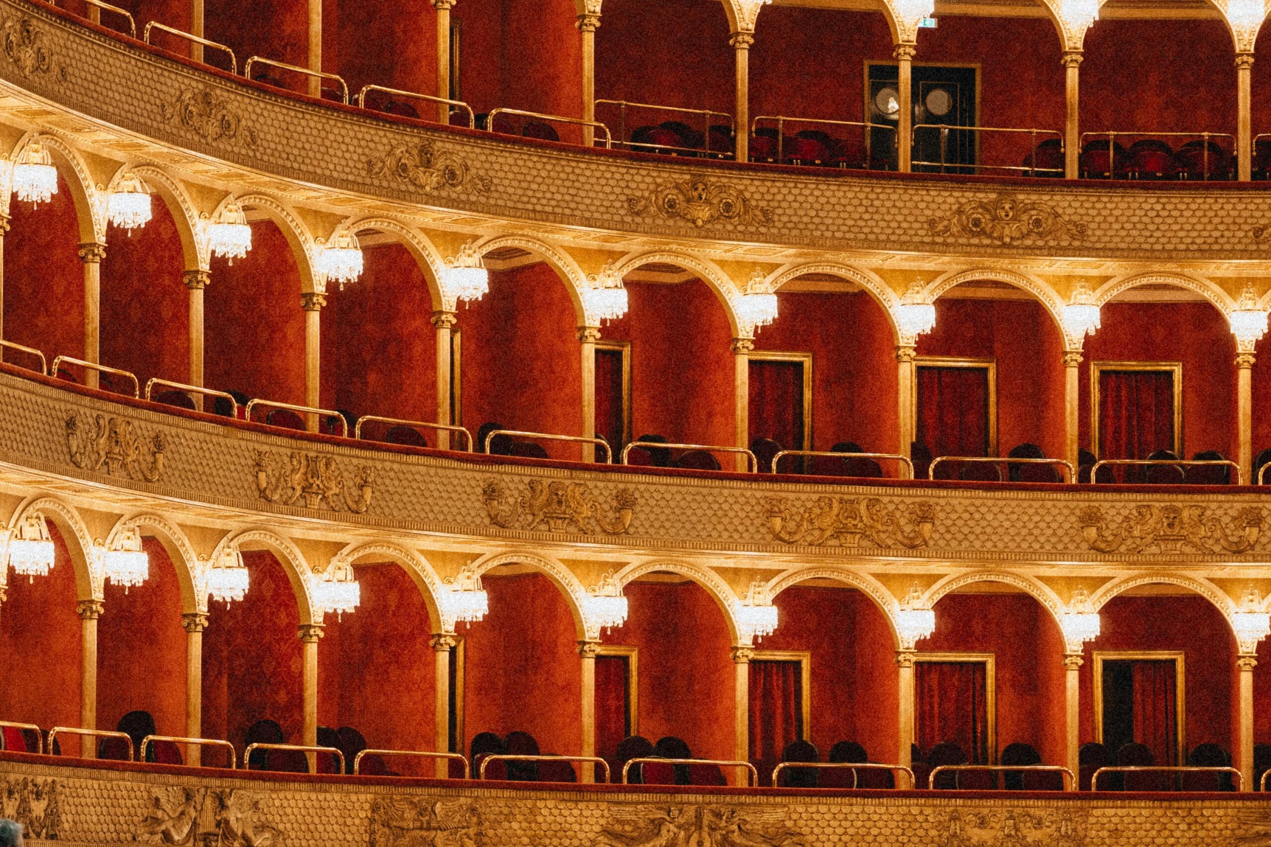 Interior de un gran teatro con paredes rojas y ventanas arqueadas, creando un ambiente elegante y acogedor.