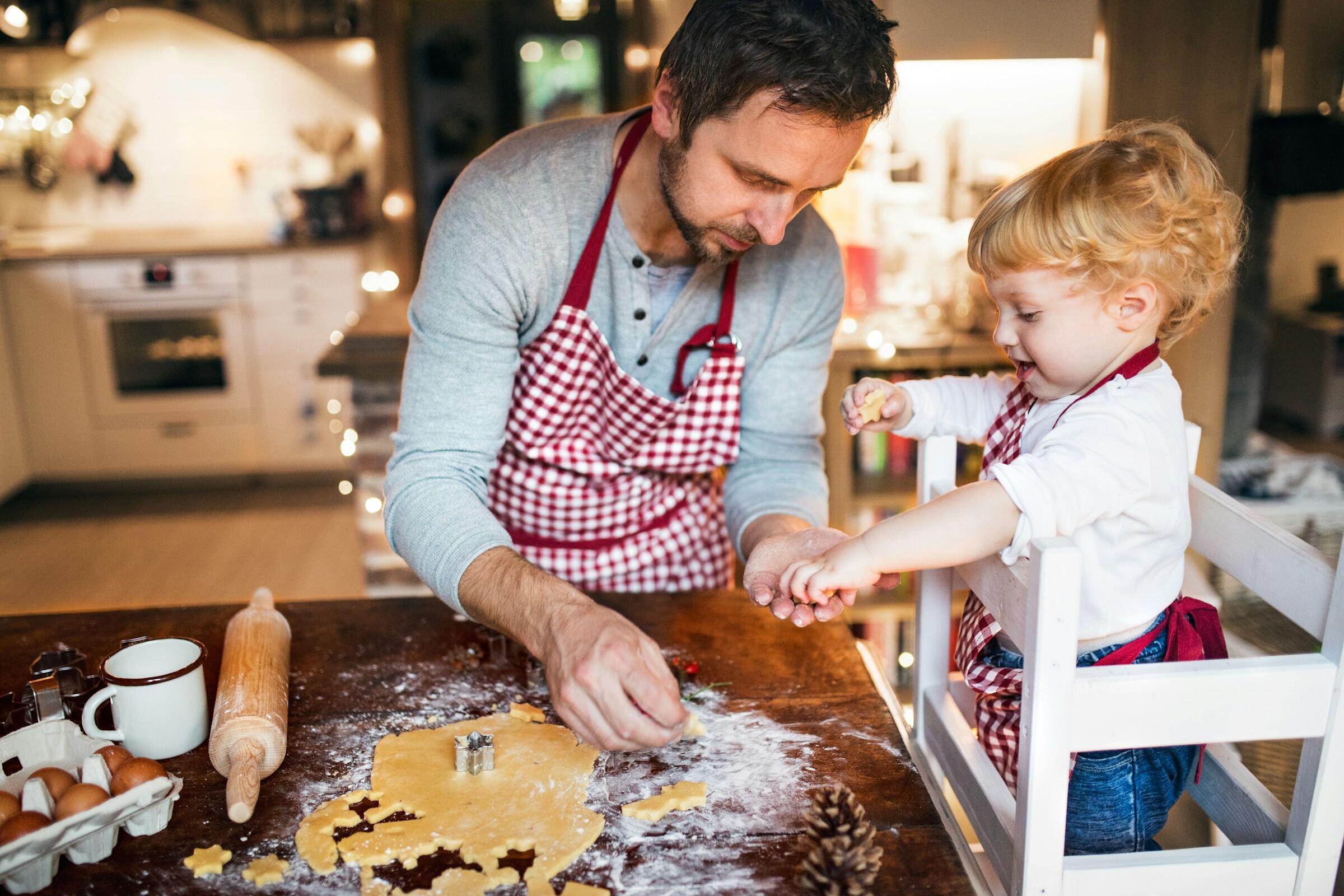 Un padre y un hijo se dedican a hornear, con harina esparcida sobre una mesa de madera, un rodillo y cortadores de galletas visibles en una acogedora cocina.