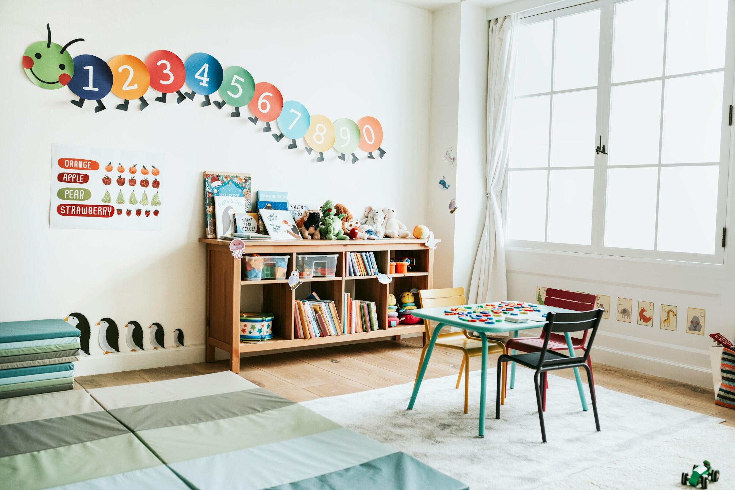Habitación infantil alegre y divertida con una colorida decoración de pared con orugas, estanterías y una mesa con juguetes educativos.