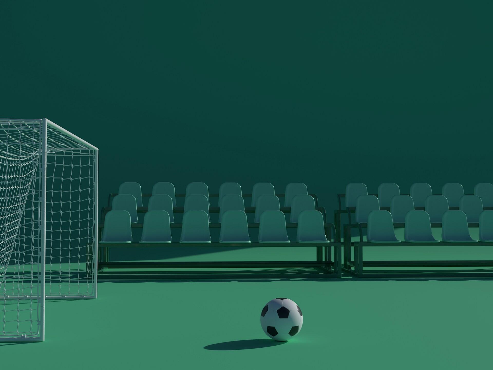 Un balón de fútbol se encuentra delante de la portería vacía de un estadio, con asientos de plástico de color verde azulado dispuestos para los espectadores en un entorno minimalista.