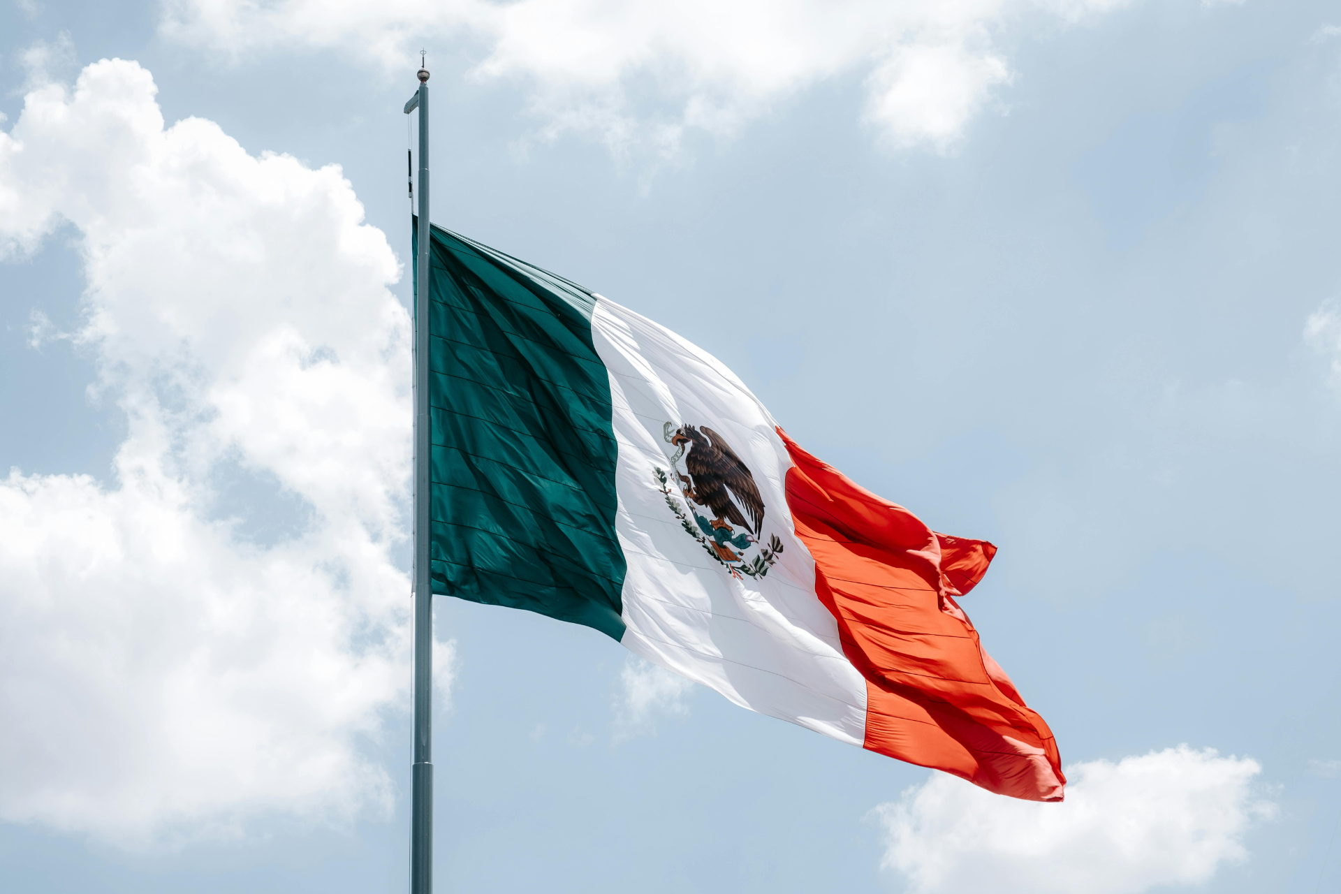 Bandera de México con tres franjas verticales de colores verde, blanco y rojo, y el escudo nacional en el centro.