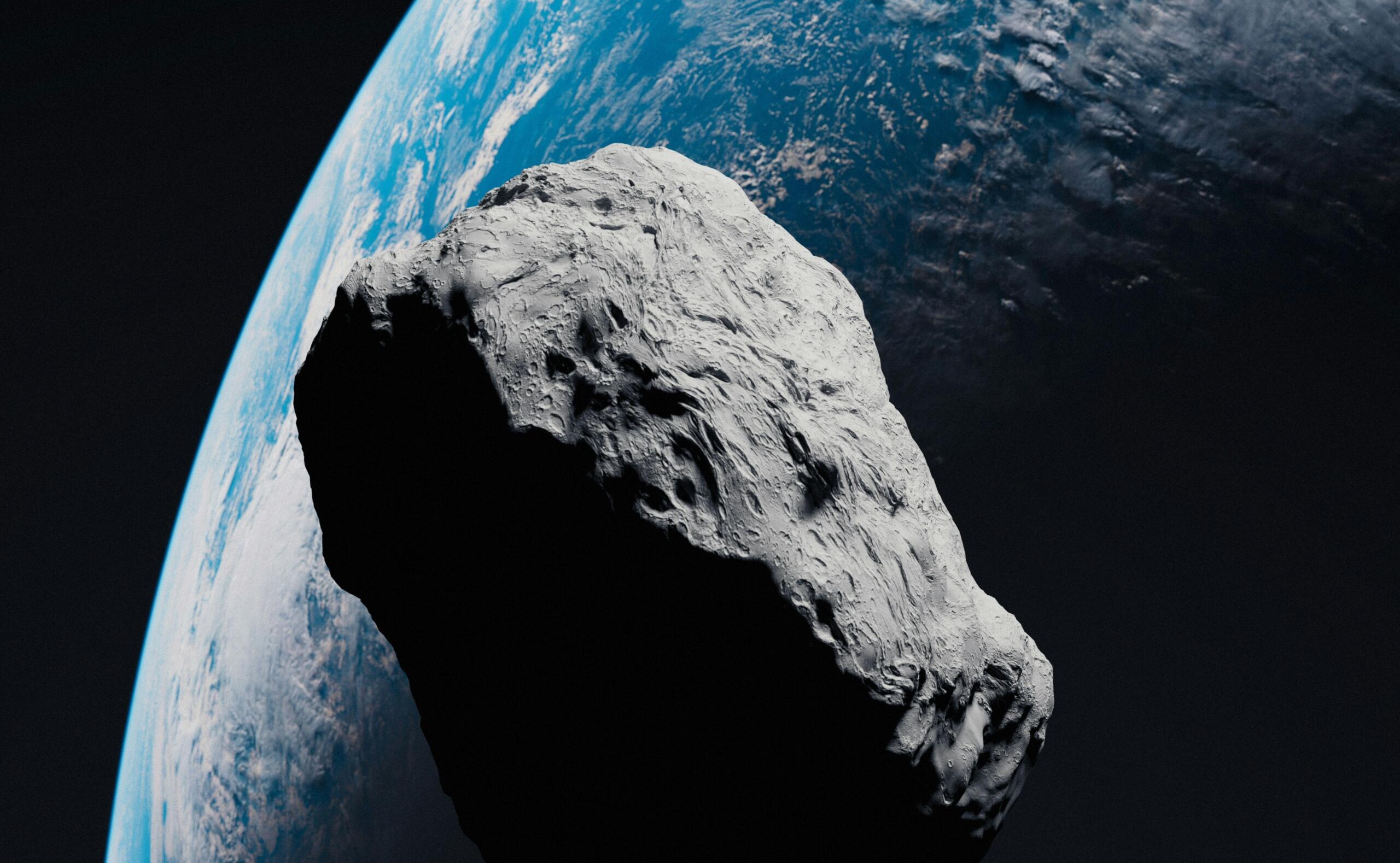 Un asteroide grande y escarpado flota en el espacio, parcialmente iluminado, con la Tierra al fondo mostrando océanos azules y nubes blancas.