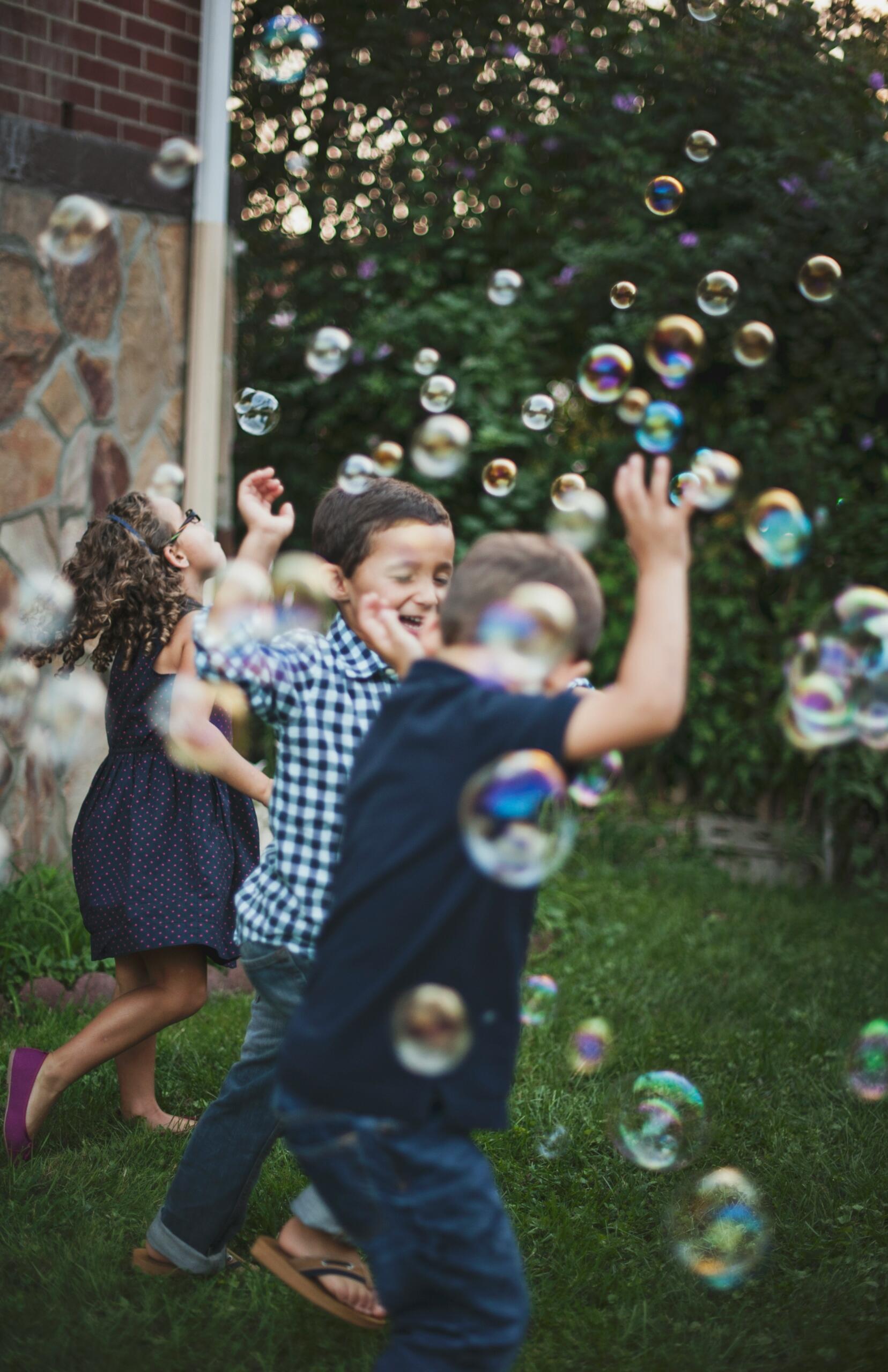 Un grupo de niños juega con burbujas en un jardín, riendo y disfrutando del aire libre.