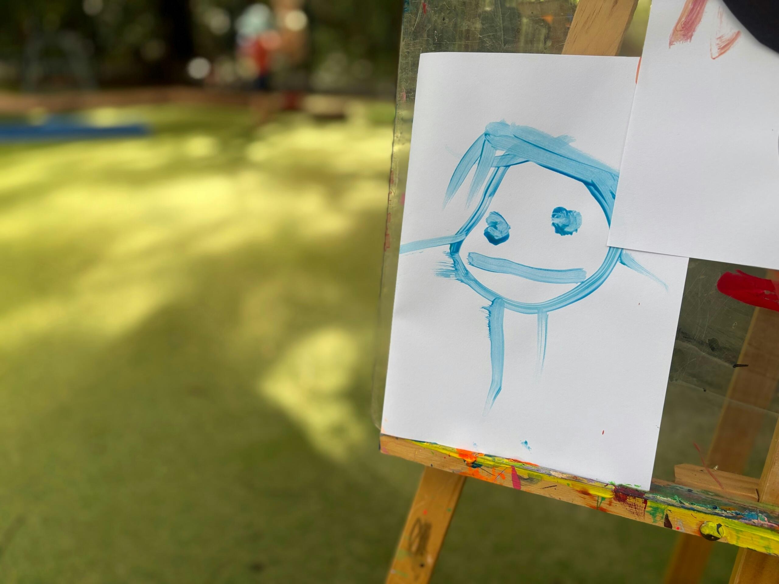 Dibujo de un rostro infantil en un caballete, mostrando una expresión alegre y colorida. 