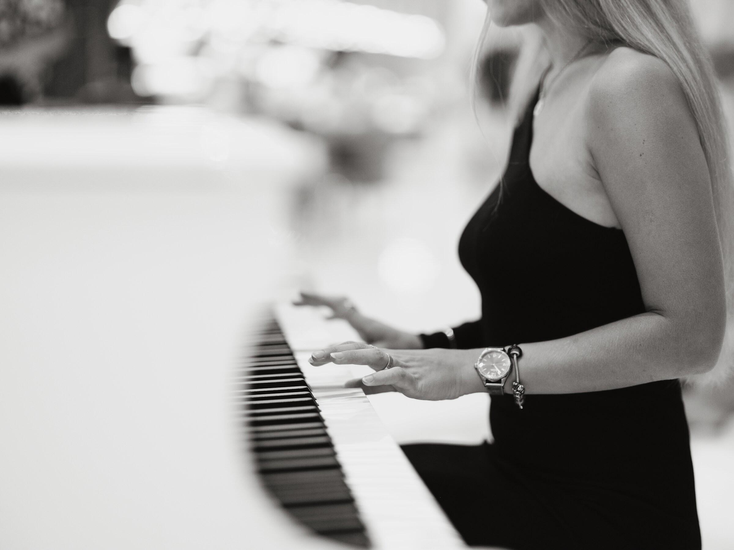 Una mujer vestida de negro toca un piano blanco, sus manos bailan con elegancia sobre las teclas, capturando un momento de arte musical.