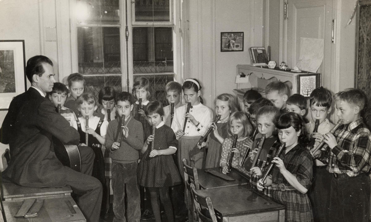 Foto en blanco y negro de un aula con niños tocando instrumentos musicales. 