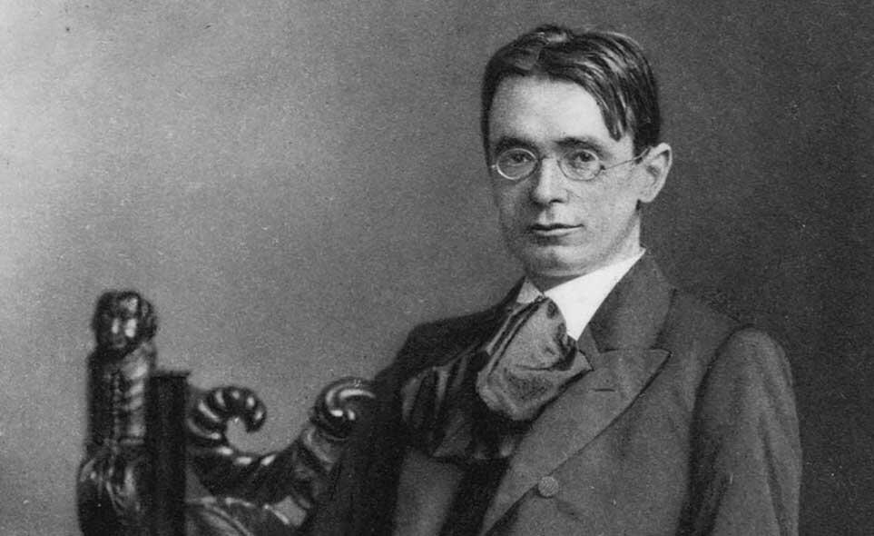 Foto en blanco y negro de un hombre vestido con traje y corbata, posando con una expresión seria. 