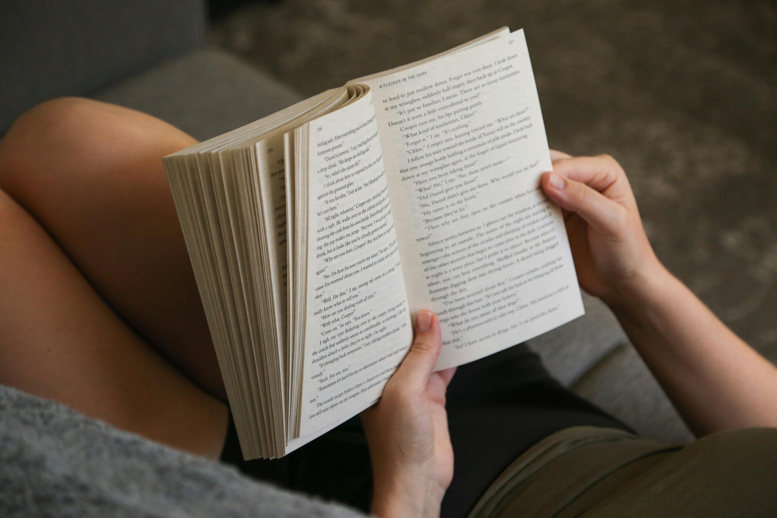 Una mujer lee un libro sentada en un sofá cómodo. 