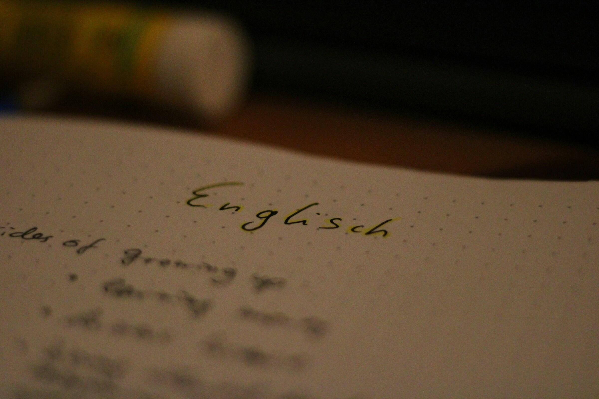 Primer plano de una página punteada de un cuaderno con la palabra «Englisch» escrita con tinta verde, rodeada de notas manuscritas con lápiz difuminado.