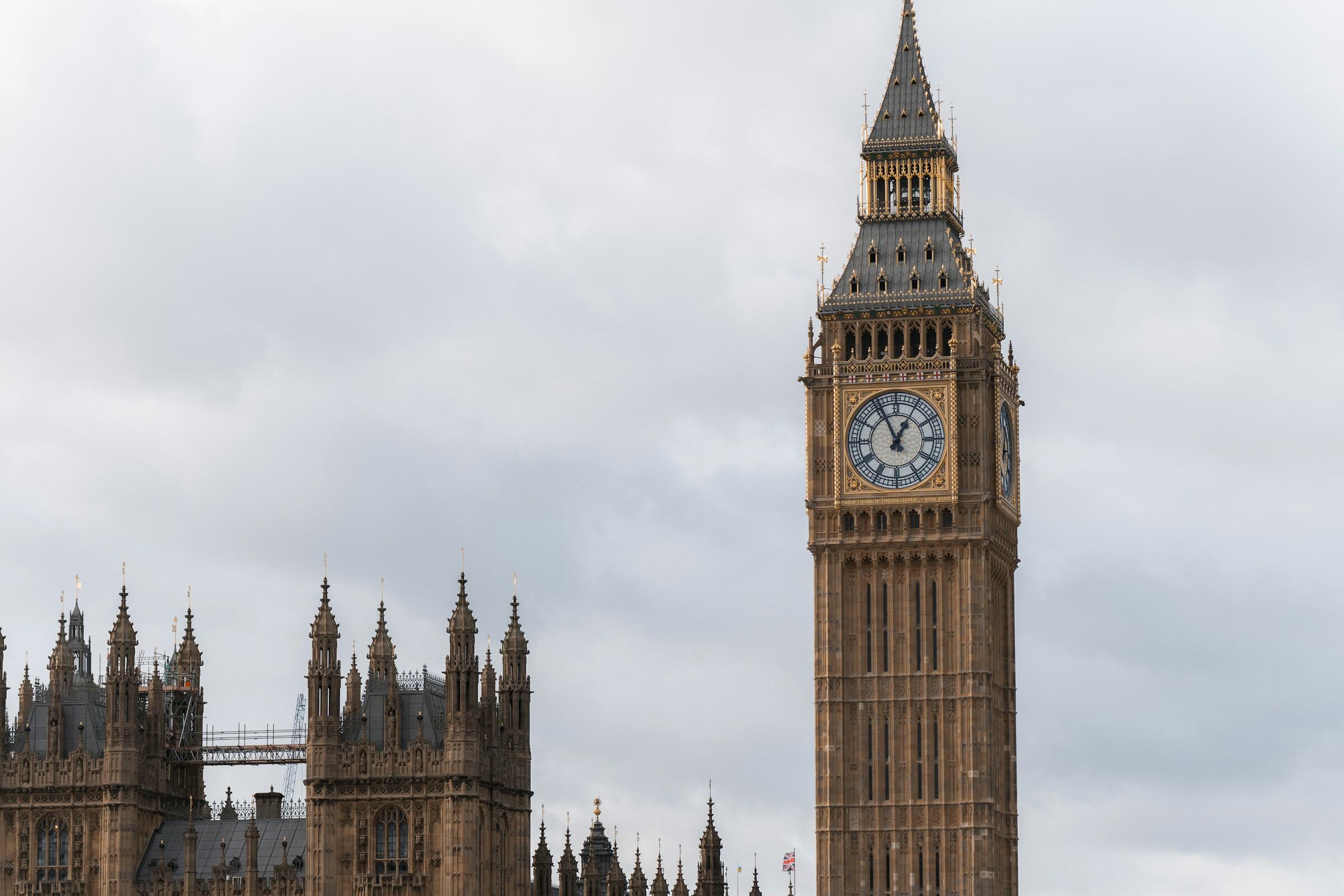 La torre del reloj Big Ben se alza imponente contra un cielo nublado, mostrando parcialmente la ornamentada arquitectura de las Casas del Parlamento cercanas.