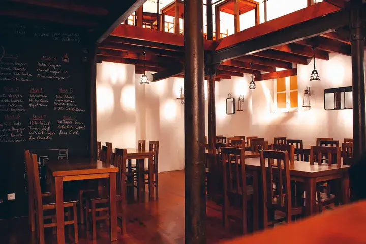 Interior de un acogedor restaurante con mesas y sillas de madera, iluminación cálida y un menú escrito en una pizarra colgada en la pared.